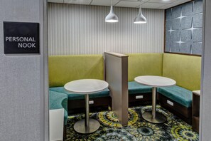 A personal nook with two tables and benches, patterned wallpaper, and pendant lighting.