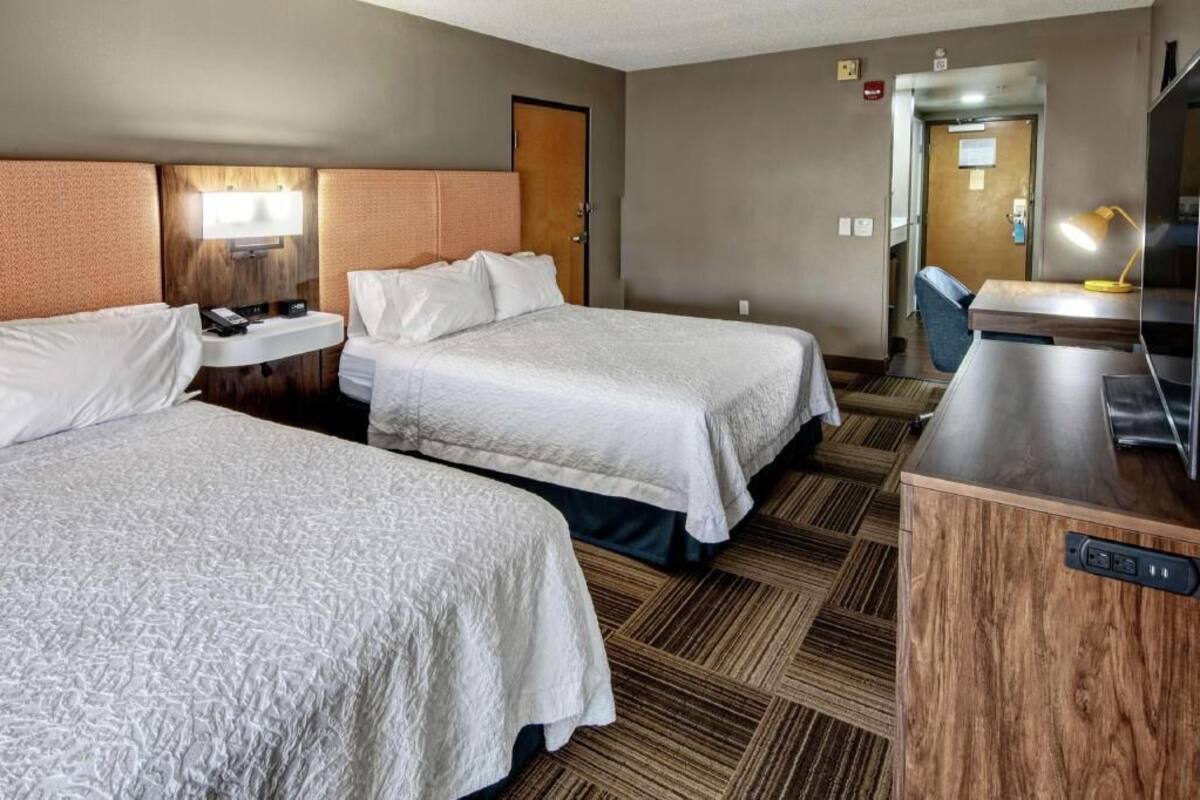 A hotel room with two beds, a desk, a chair, and a television.