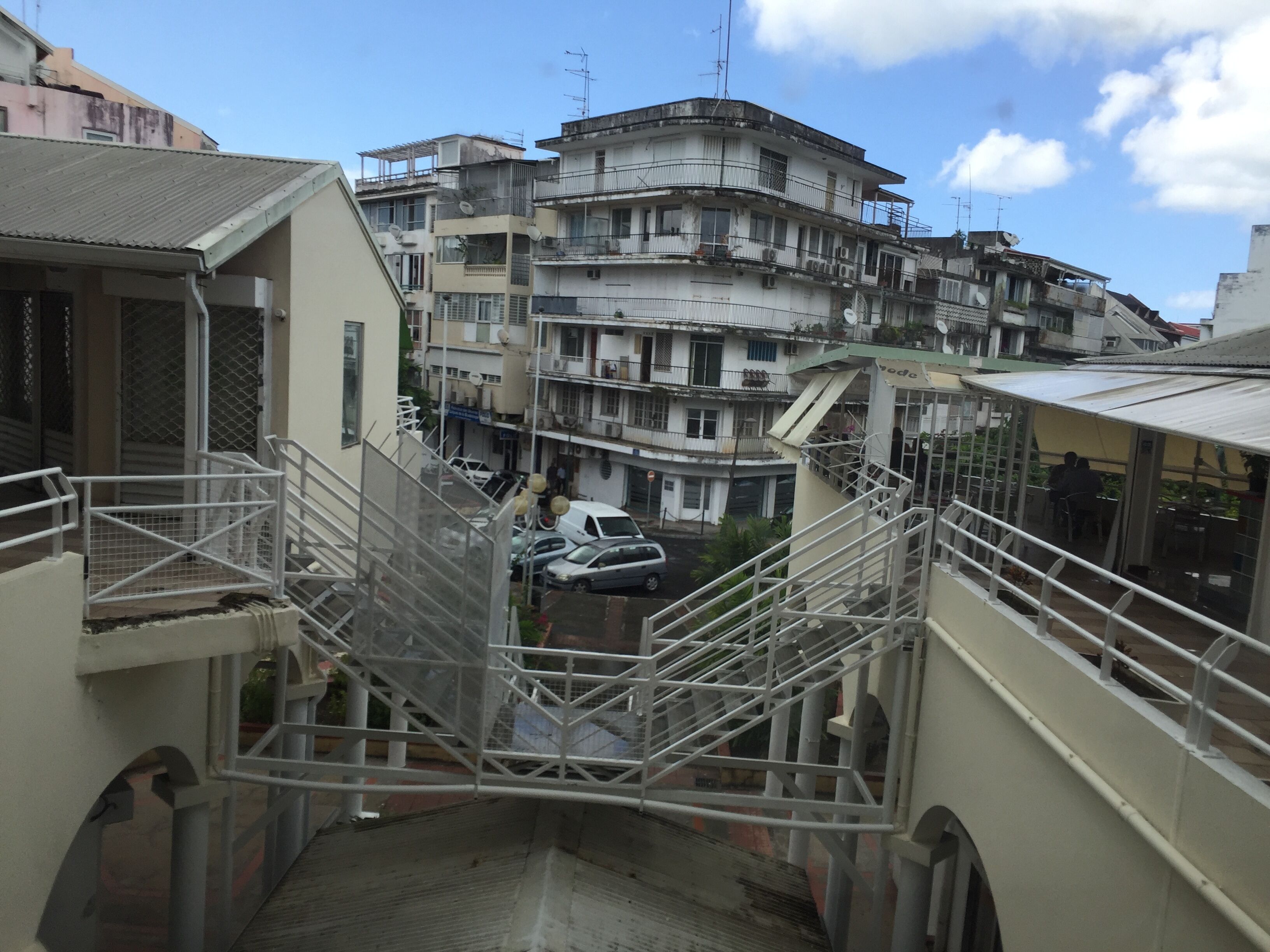 Un edificio residencial de varios pisos con balcones, una escalera y coches estacionados.