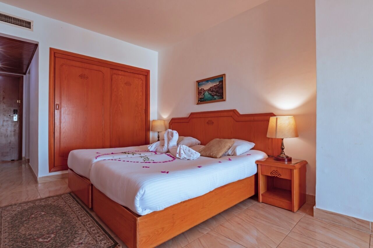 A hotel room with a wooden bed, two bedside lamps, a painting on the wall, and a large wardrobe.