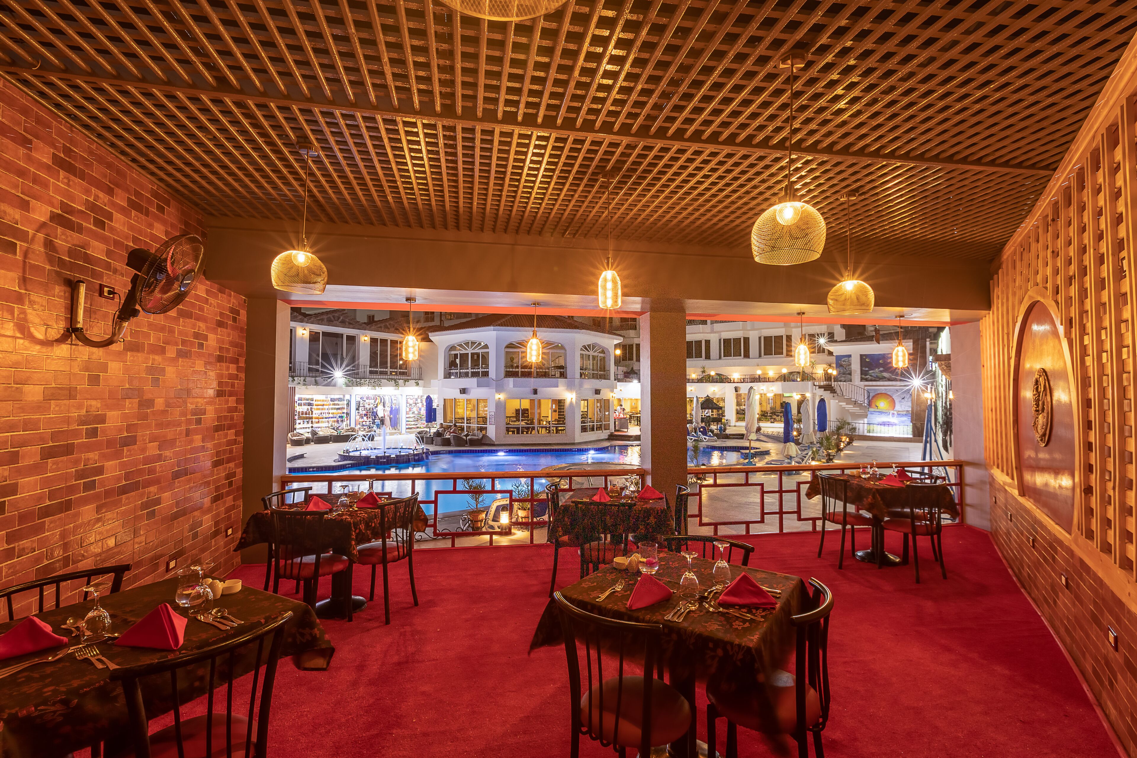 Un espace de restauration intérieur avec des murs en briques, un sol recouvert d’une moquette rouge et des tables dressées pour le repas.