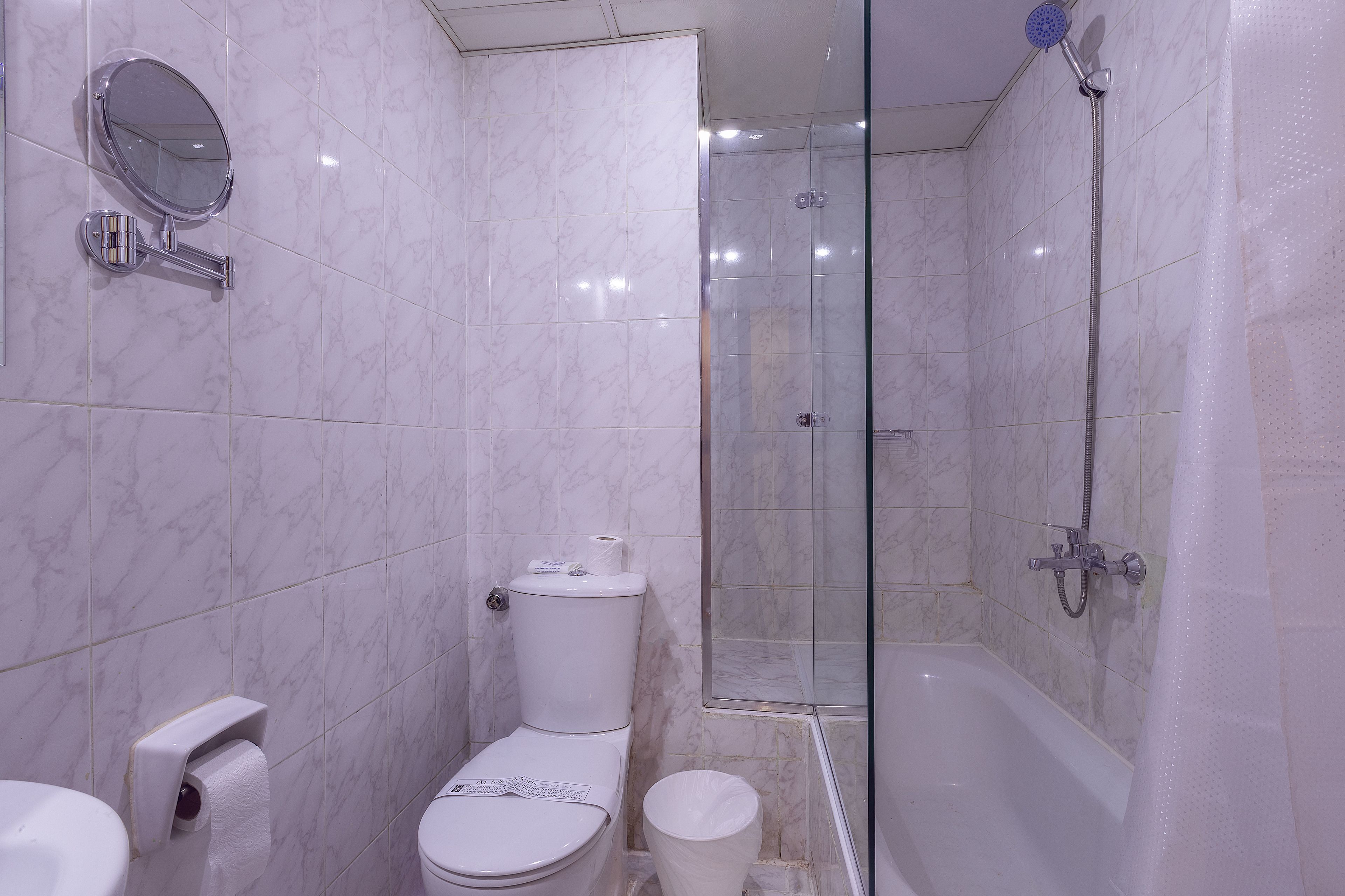 Een badkamer met toilet, een hygiëneschuimer, douche en een douchecabine met glazen wanden.