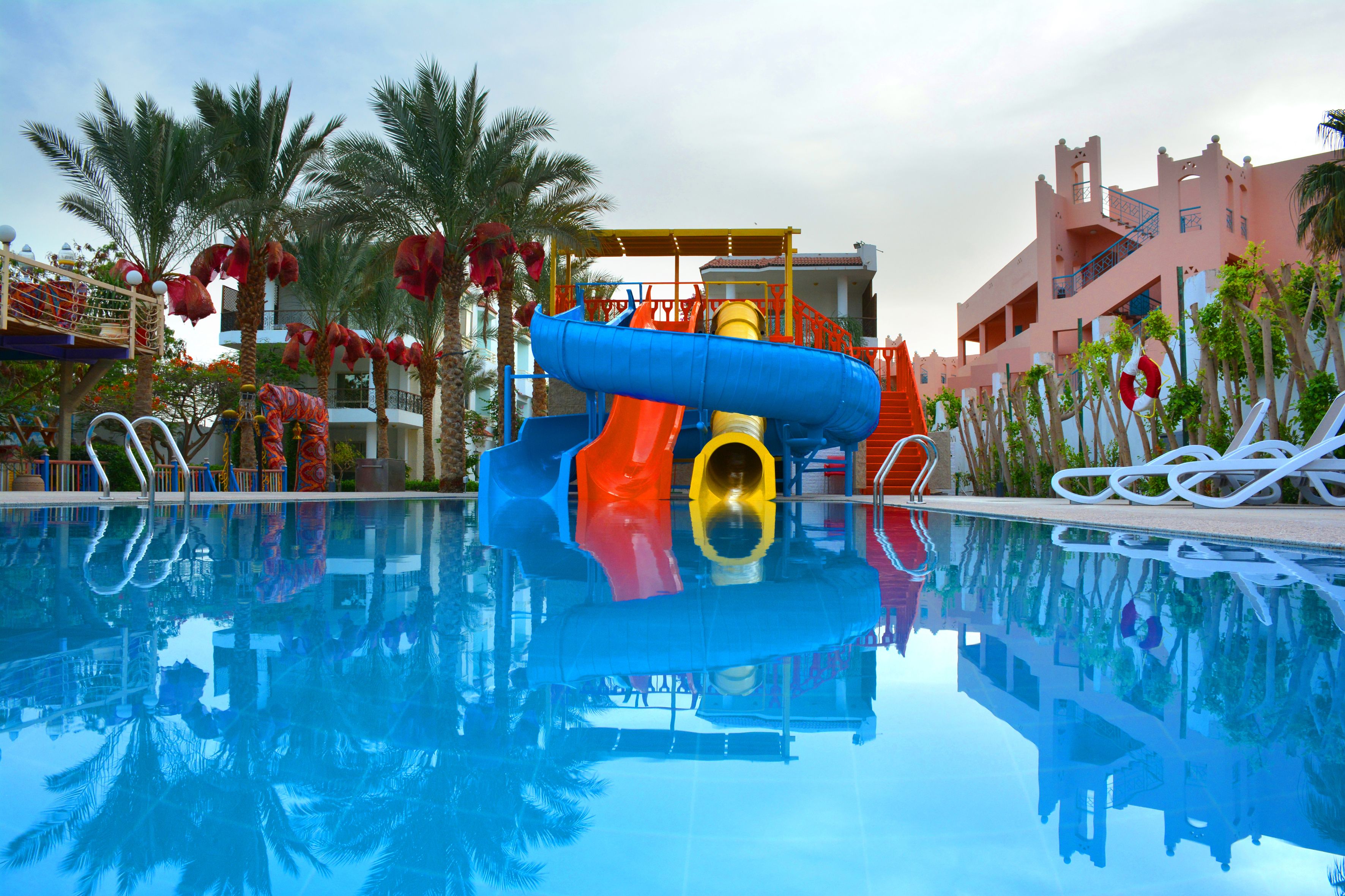Une piscine avec un toboggan, des palmiers et un bâtiment doté de balcons.