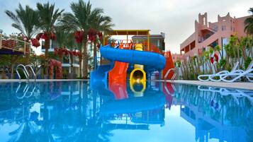 Une piscine avec un toboggan, des palmiers et un bâtiment doté de balcons.