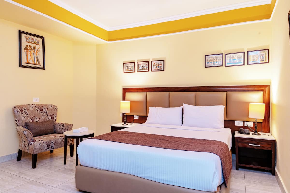 A hotel room with a bed, a chair, a nightstand, and wall art.