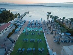 Um hotel à beira-mar com área de piscina, espreguiçadeiras, guarda-sóis e vista para o mar.