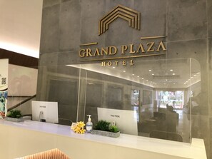 A reception desk at Grand Plaza Hotel with a modern design, a clear glass partition, and a sign indicating the hotel name. - Grand Plaza Hotel (Tamuning)