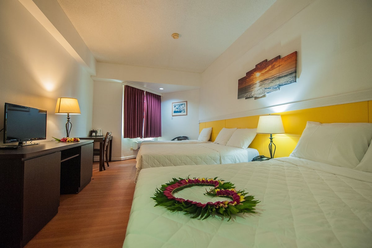 Quarto de hotel com duas camas, uma secretária com televisão e um espaço para refeições.