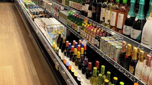 A refrigerated aisle in a store with various bottles of beverages, including wine and spirits, neatly arranged on shelves. - Grand Plaza Hotel (Tamuning)