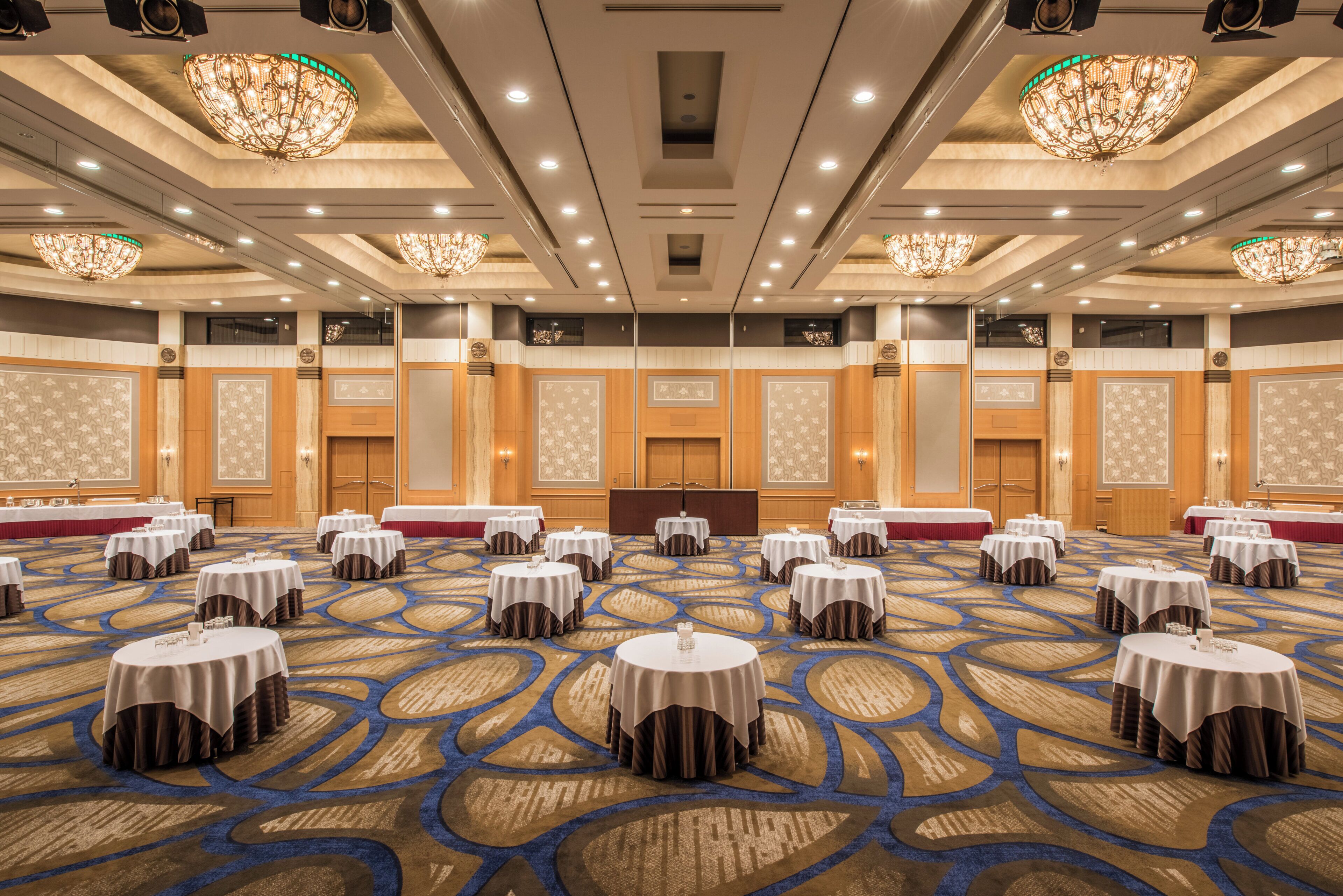 A large conference room with round tables, a podium, and a carpeted floor.