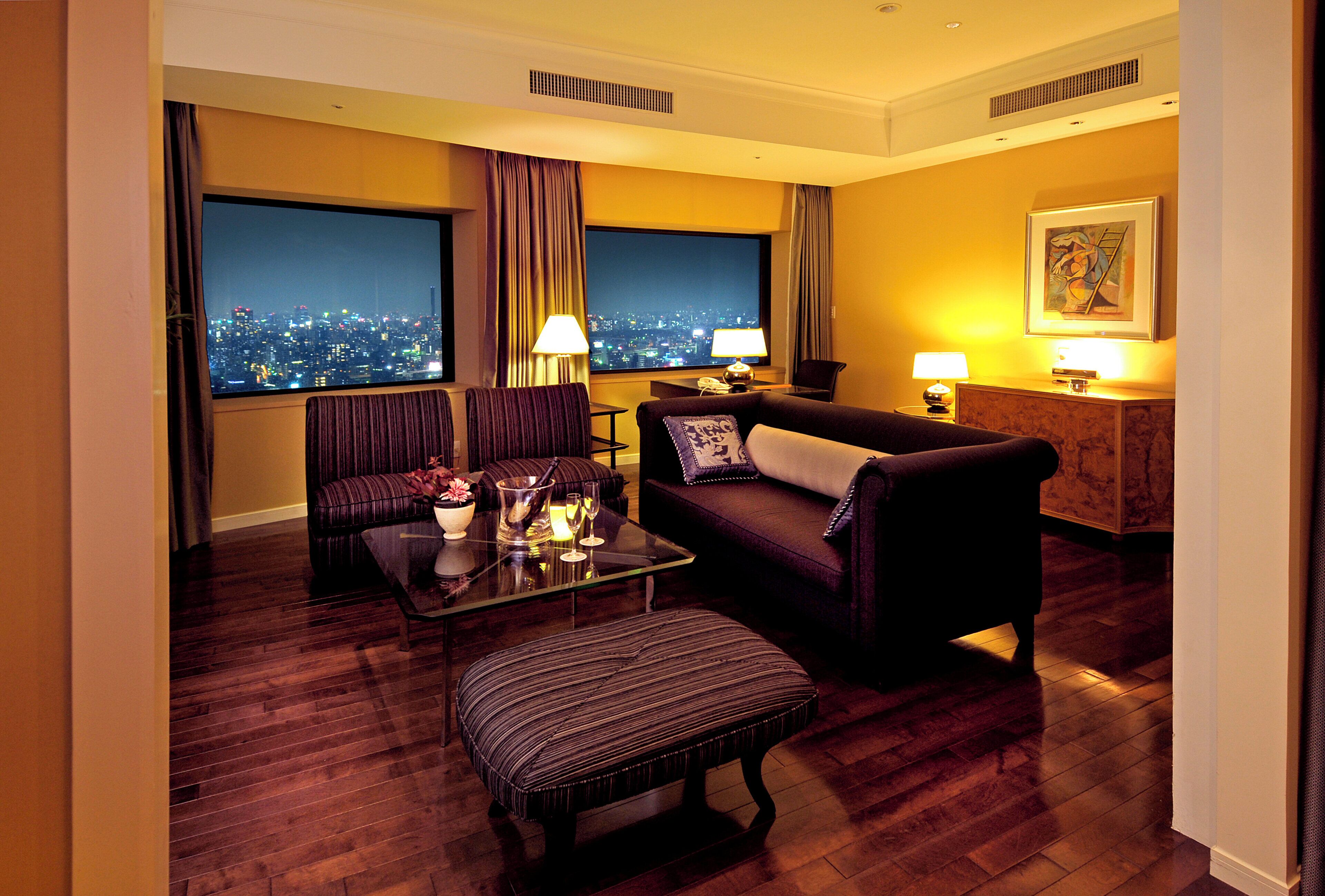 Une chambre d’hôtel avec vue sur la ville, comprenant un canapé, un fauteuil, une table et une lampe.