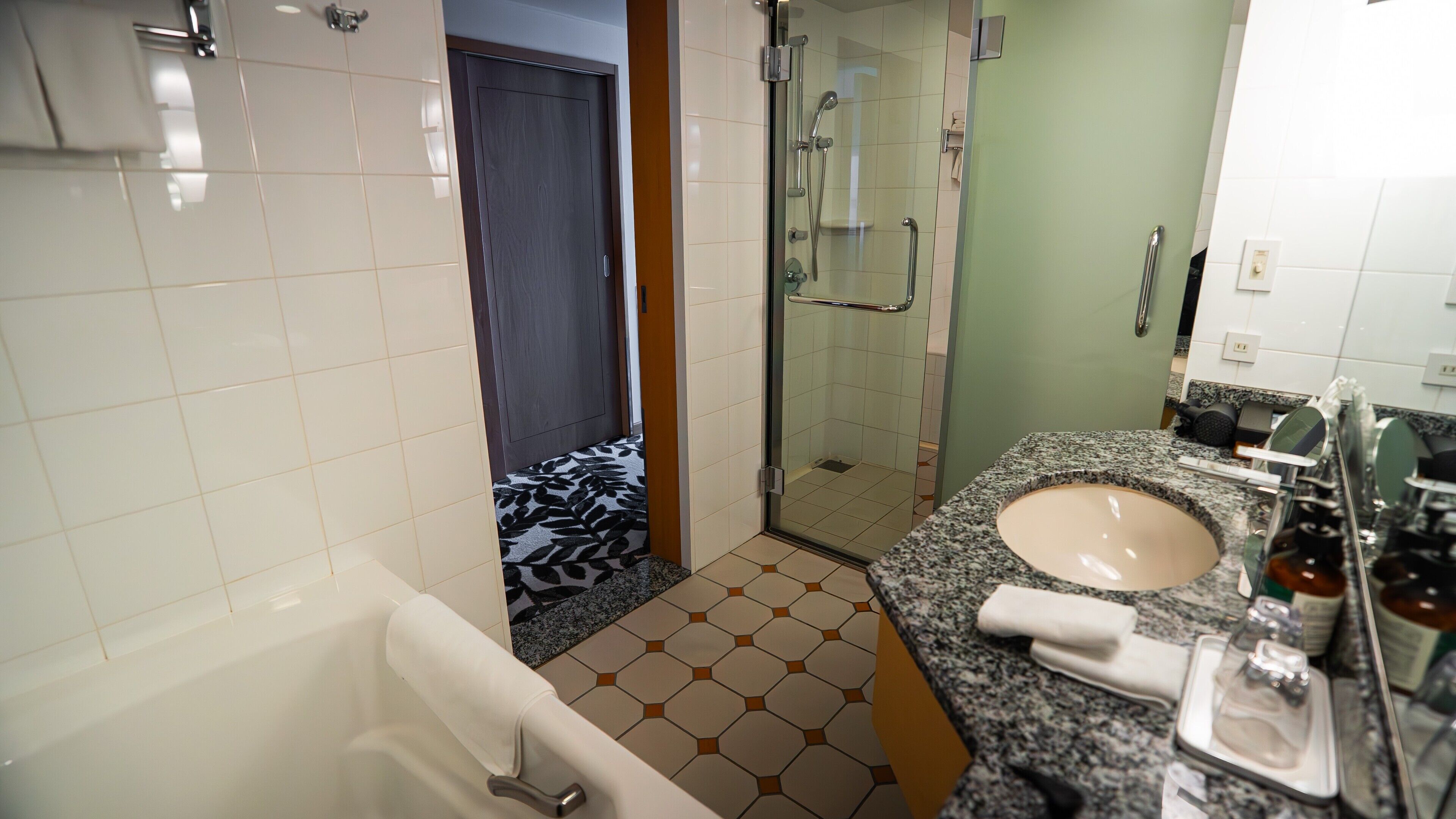 Une salle de bain avec une baignoire, une douche, un lavabo doté d’un plan de travail en granit et un miroir.