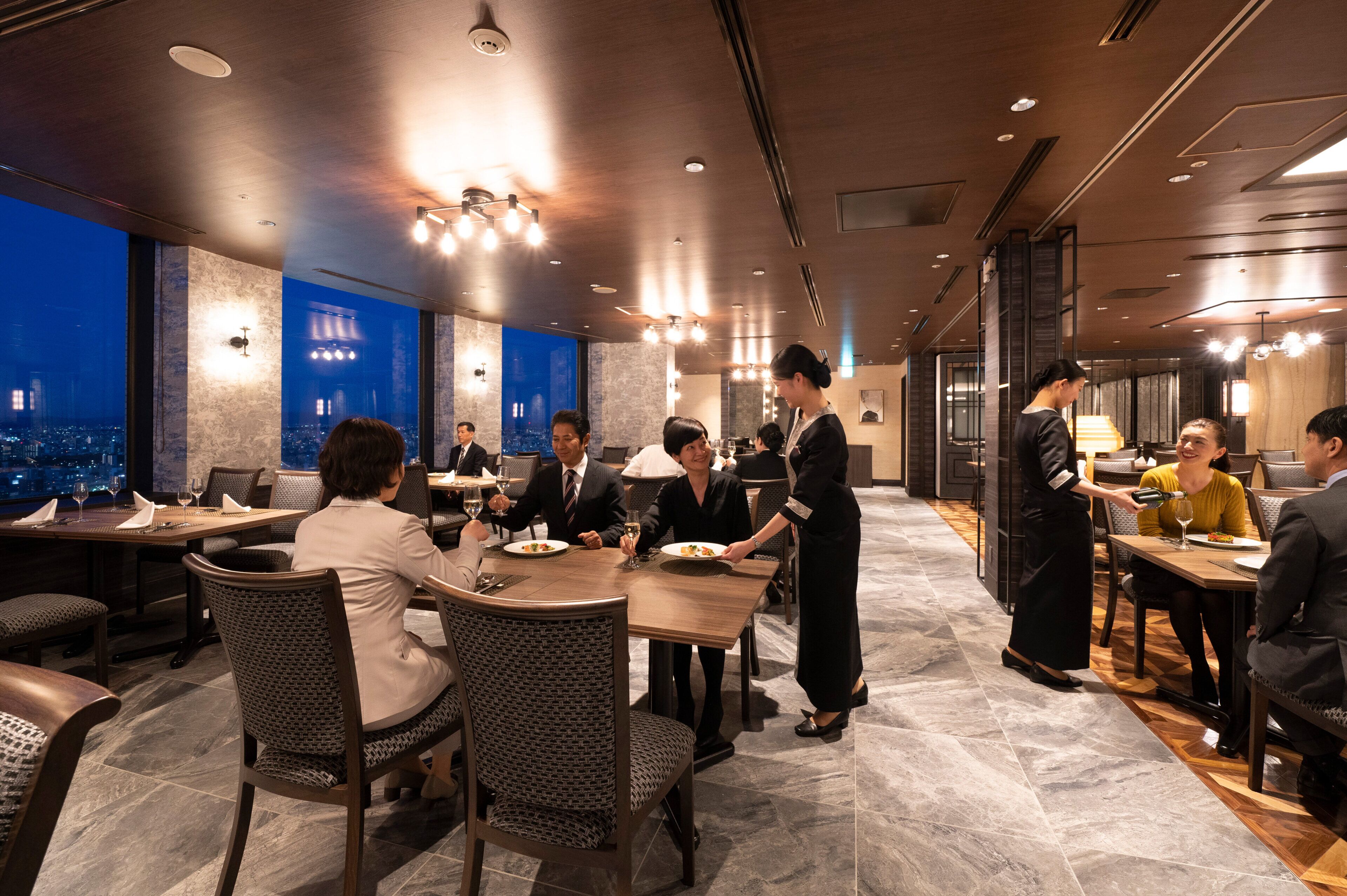 A modern dining area with multiple tables, chairs, and a view of the cityscape through large windows.