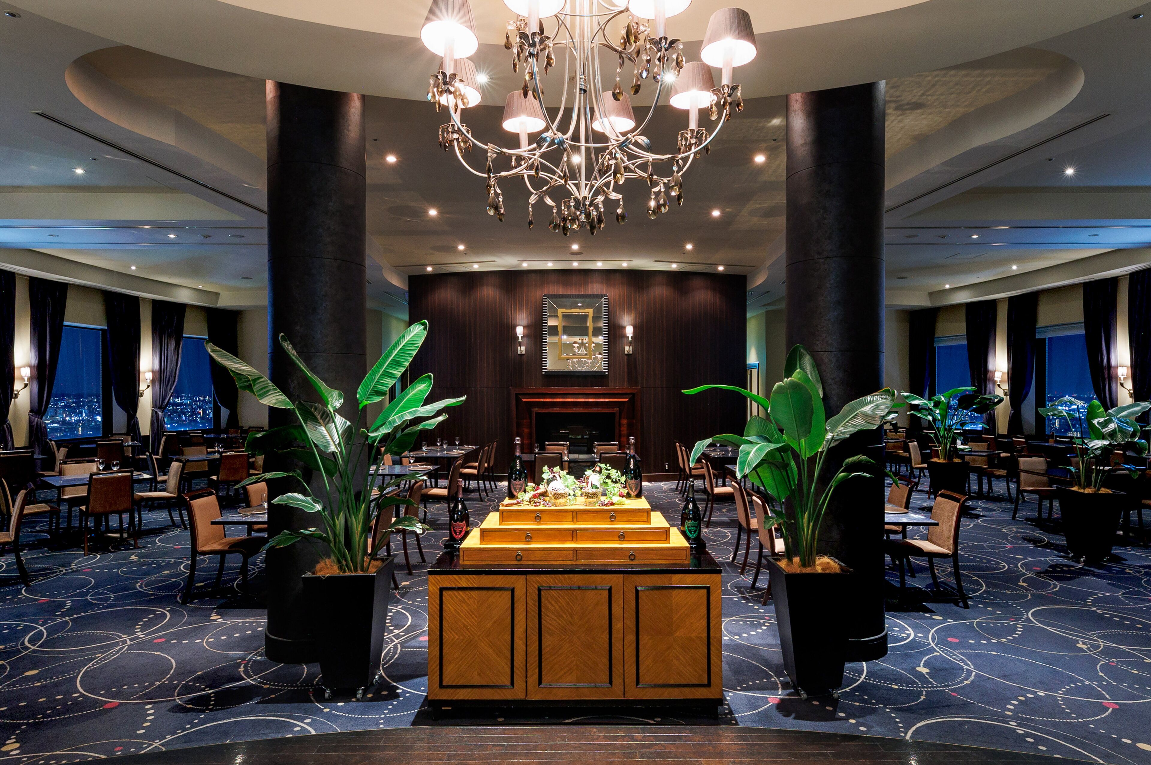 Eine geräumige Hotelhalle mit einer zentralen Bar, großen Kübelpflanzen und einem Chandelier.