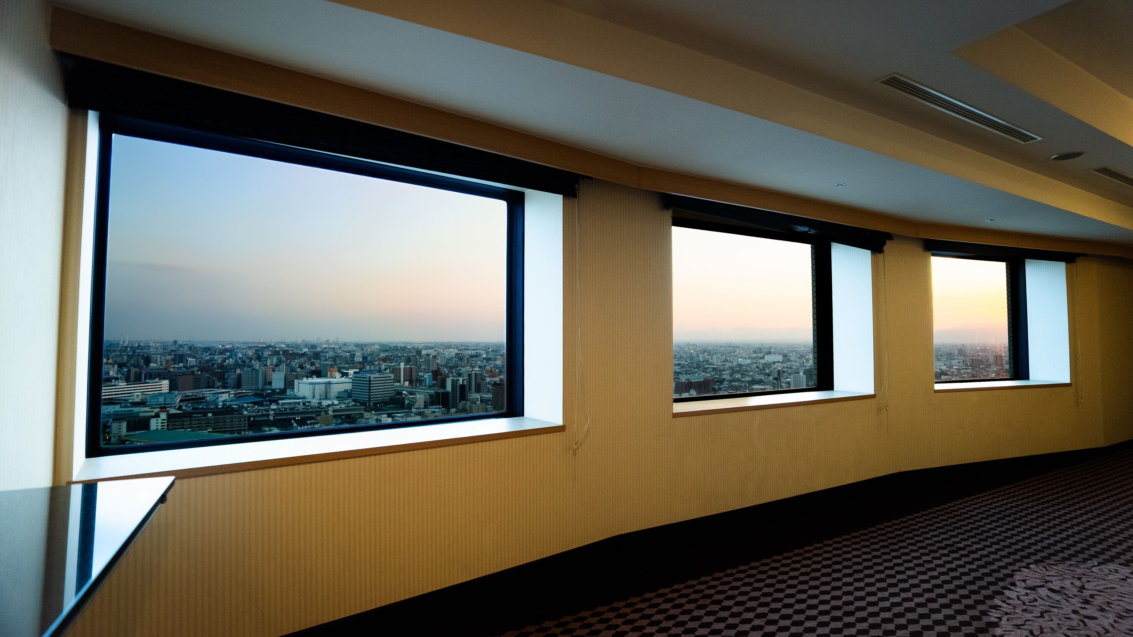 Un pasillo de hotel con amplios ventanales que ofrecen vistas de la ciudad.