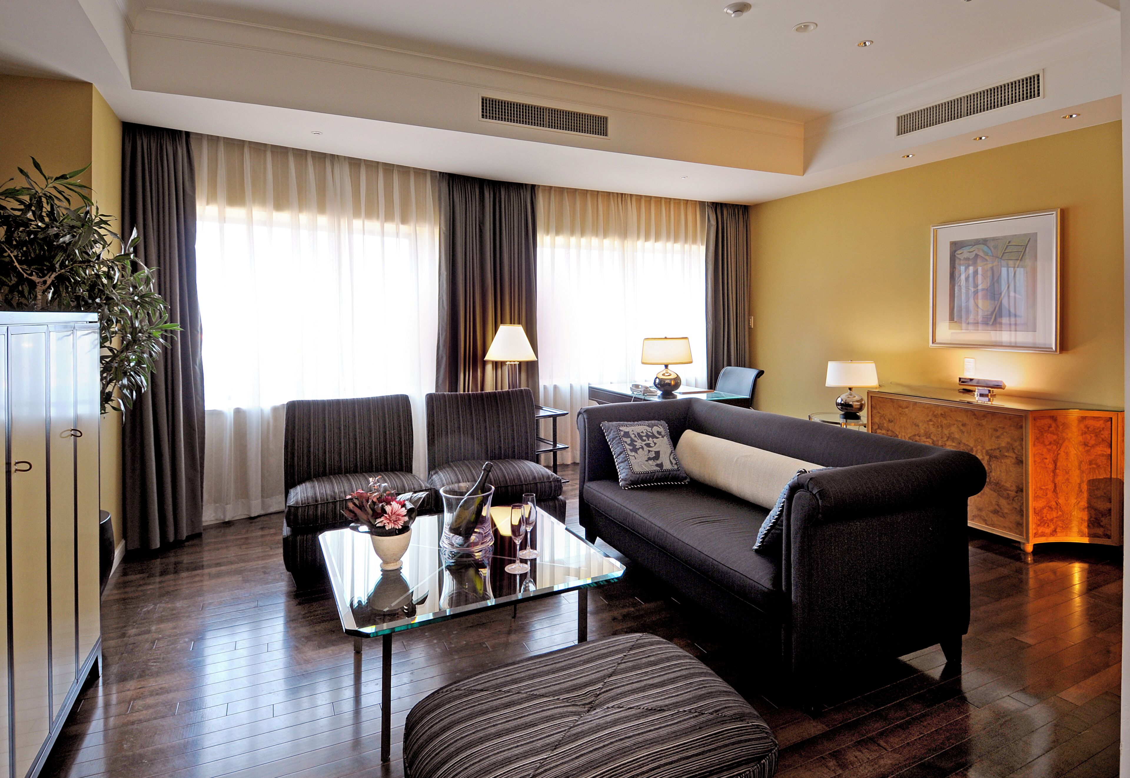 A modern living room with a sofa, armchairs, a glass coffee table, and a dining area with a lamp.