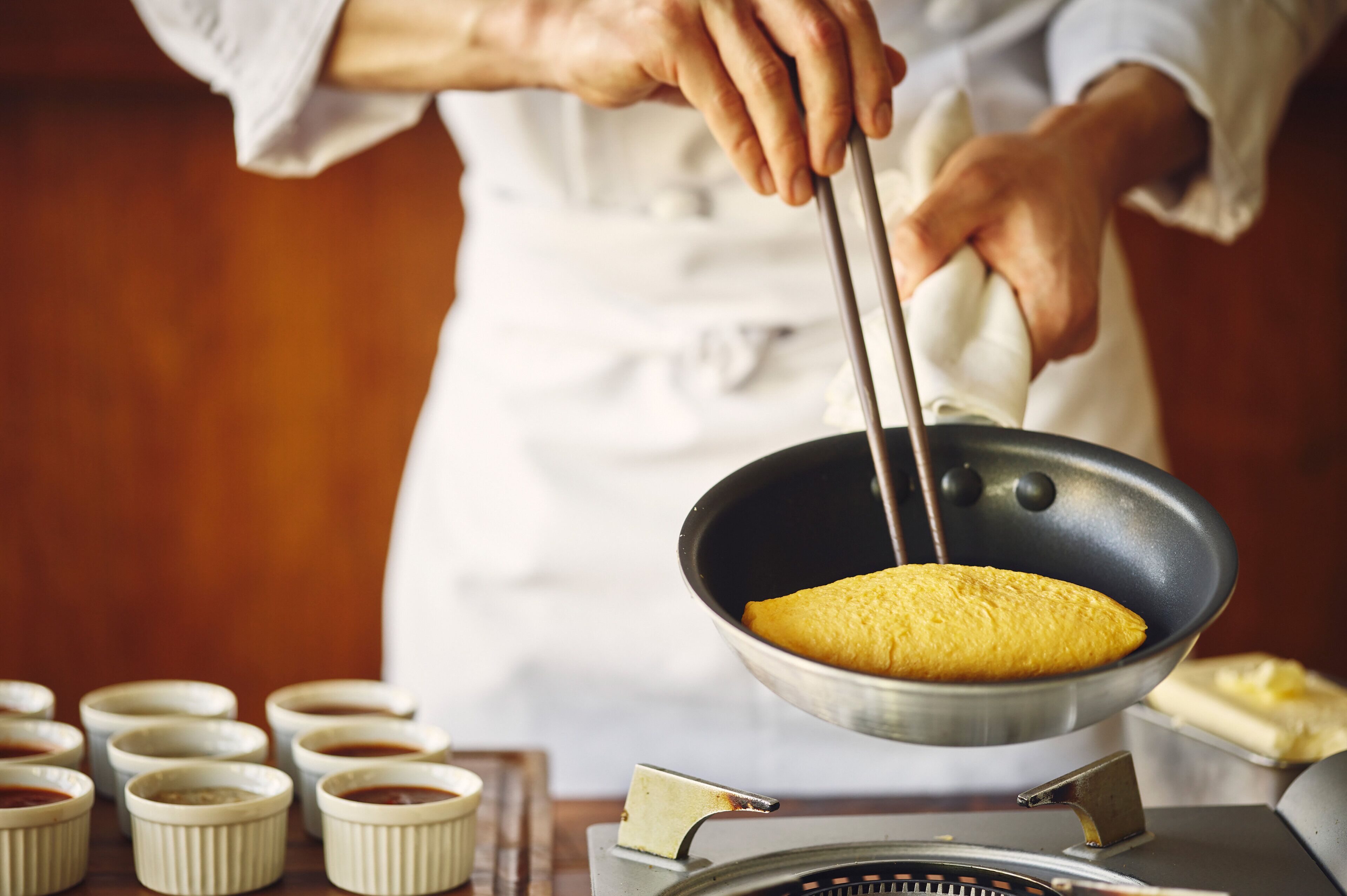 A person cooking in a kitchen with a frying pan and several small bowls.