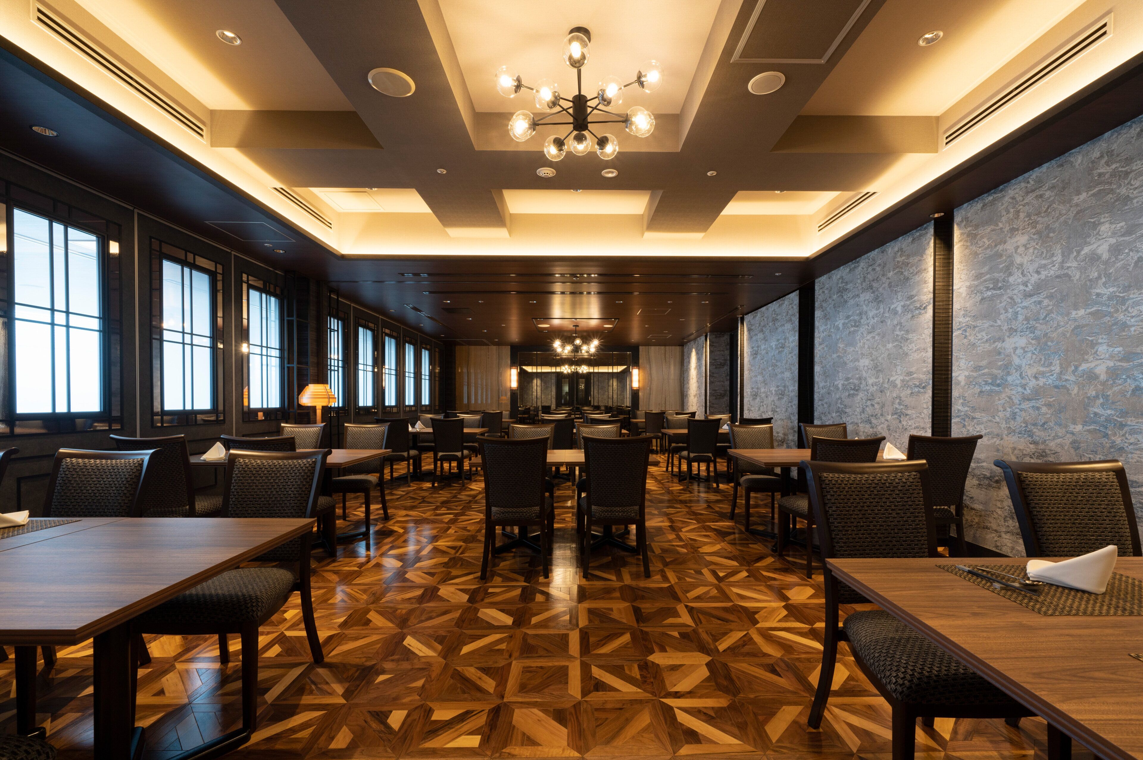 A spacious dining area with multiple tables and chairs, large windows, and a patterned floor.