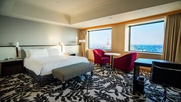 Habitación de hotel con una cama grande, un sillón rojo, una mesita redonda y un escritorio con una computadora.