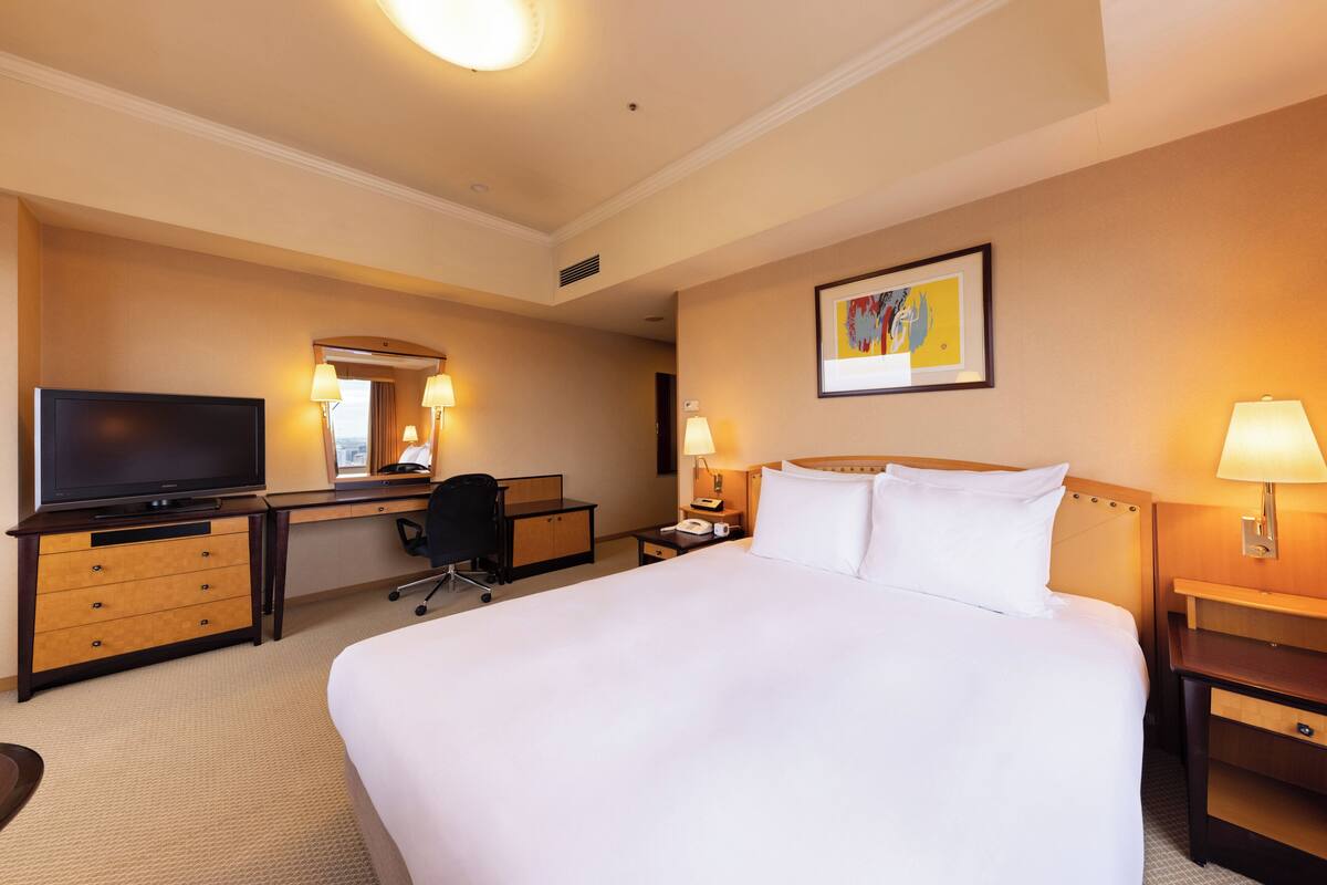 Una habitación de hotel con una cama grande, un escritorio con silla, un televisor y una lámpara de escritorio.