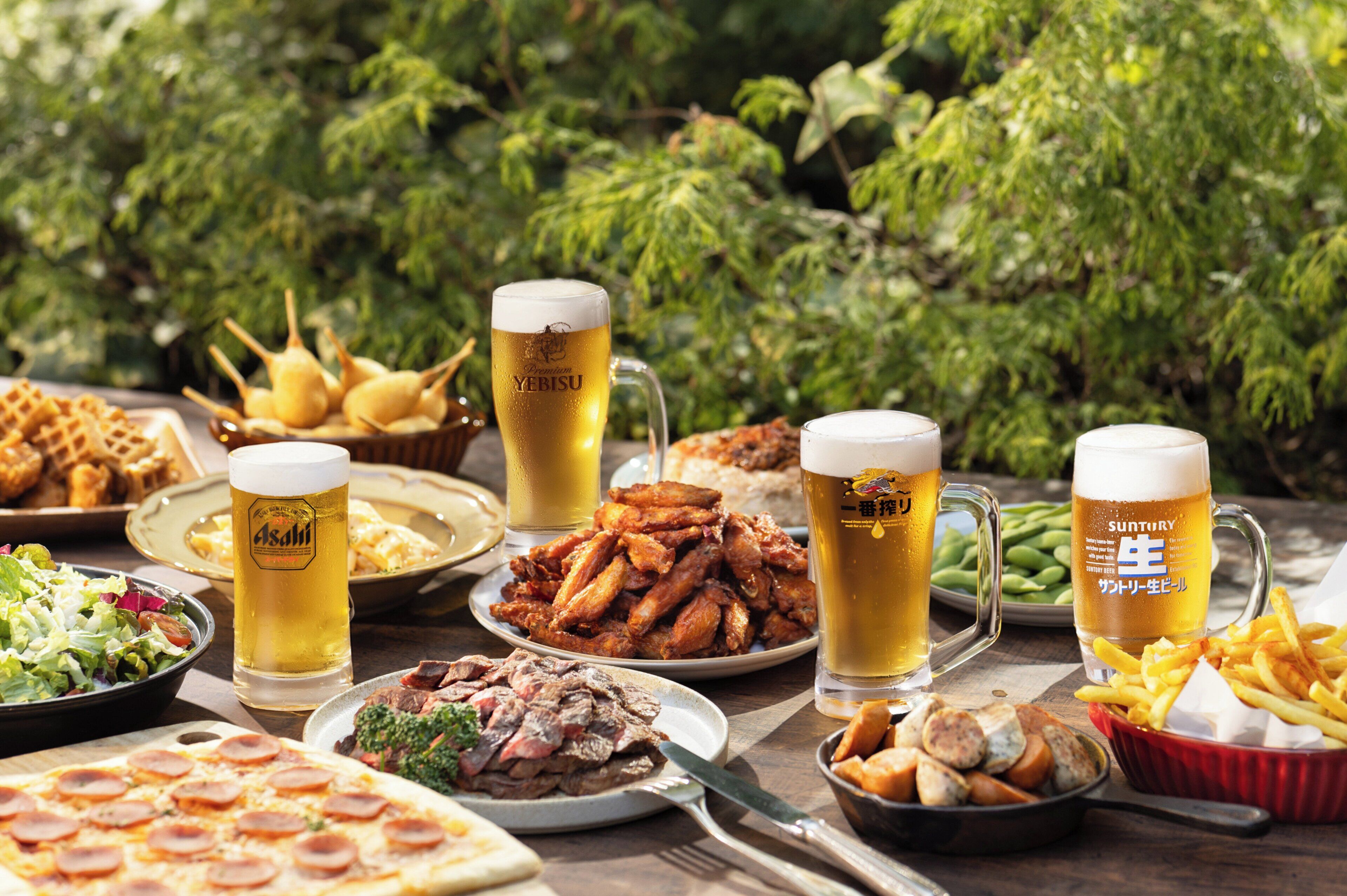 A table with various dishes and beer glasses, surrounded by greenery.
