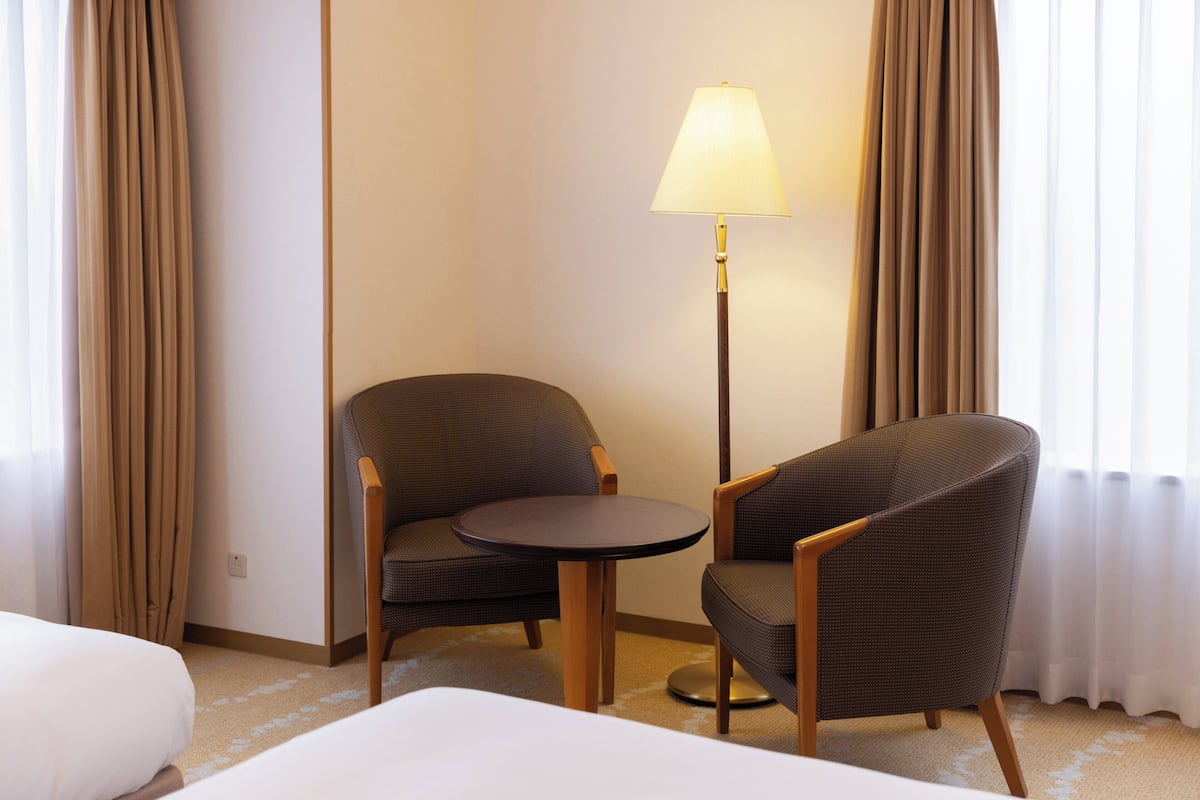 Habitación de hotel con una cama, dos sillones, una mesita redonda, una lámpara y cortinas.