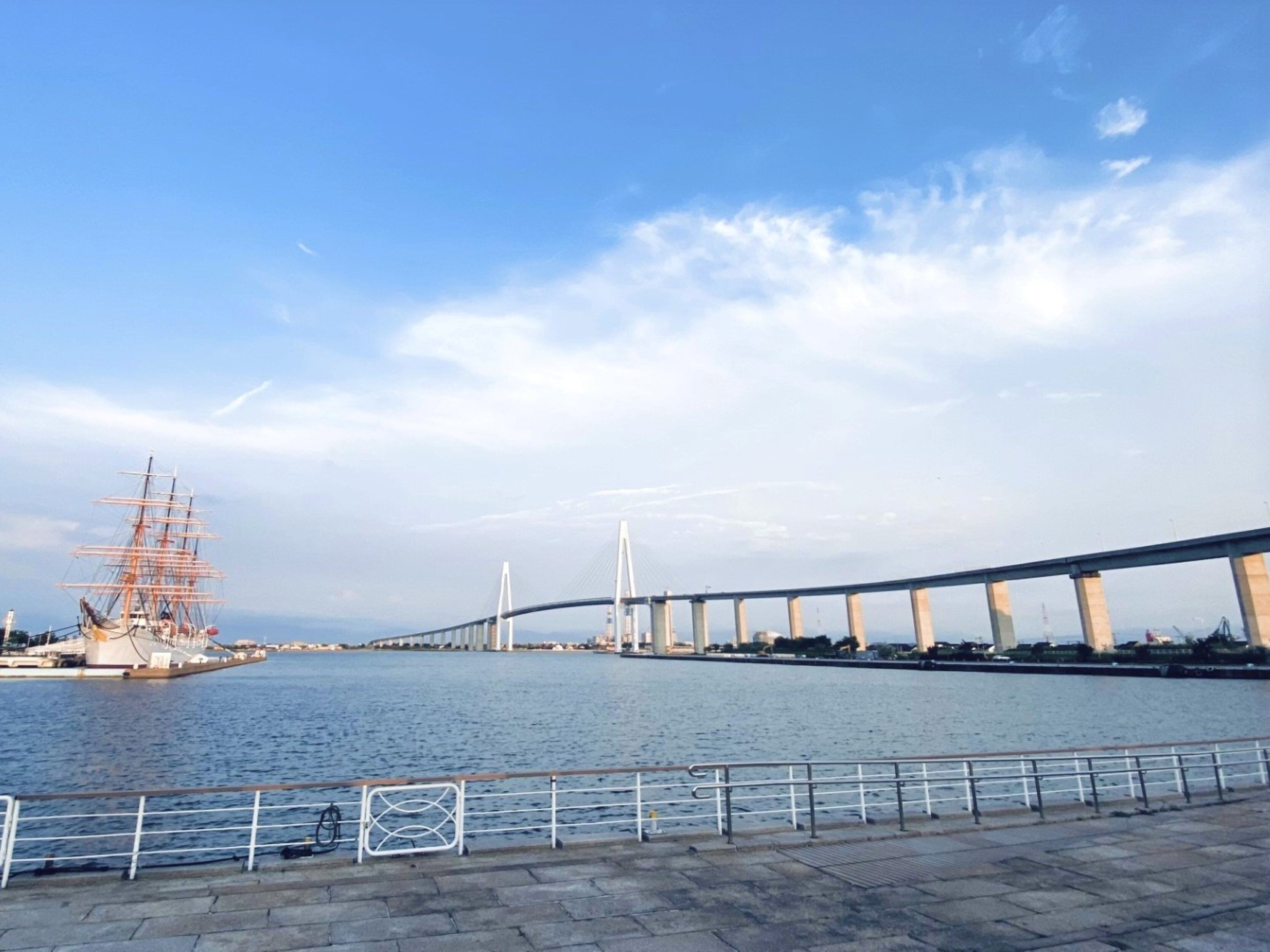 A river with a bridge and a tall ship docked on the left.