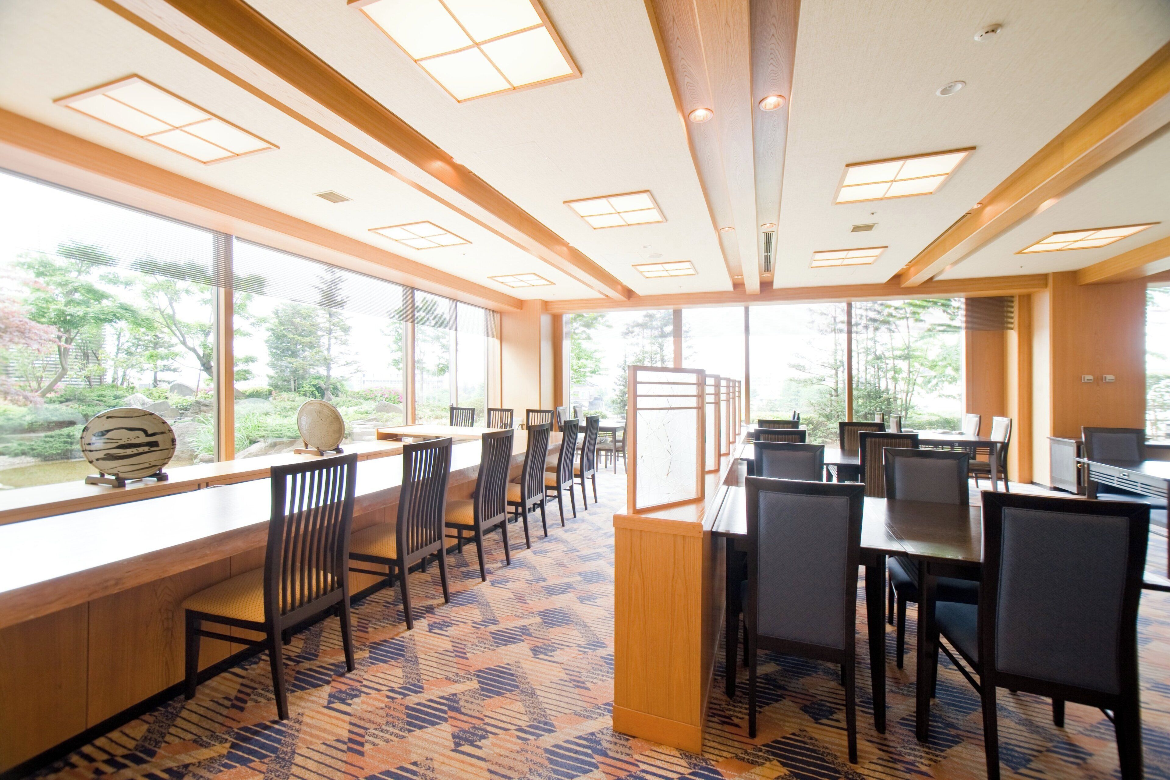 A spacious dining area with large windows, wooden ceiling beams, and a patterned carpet.