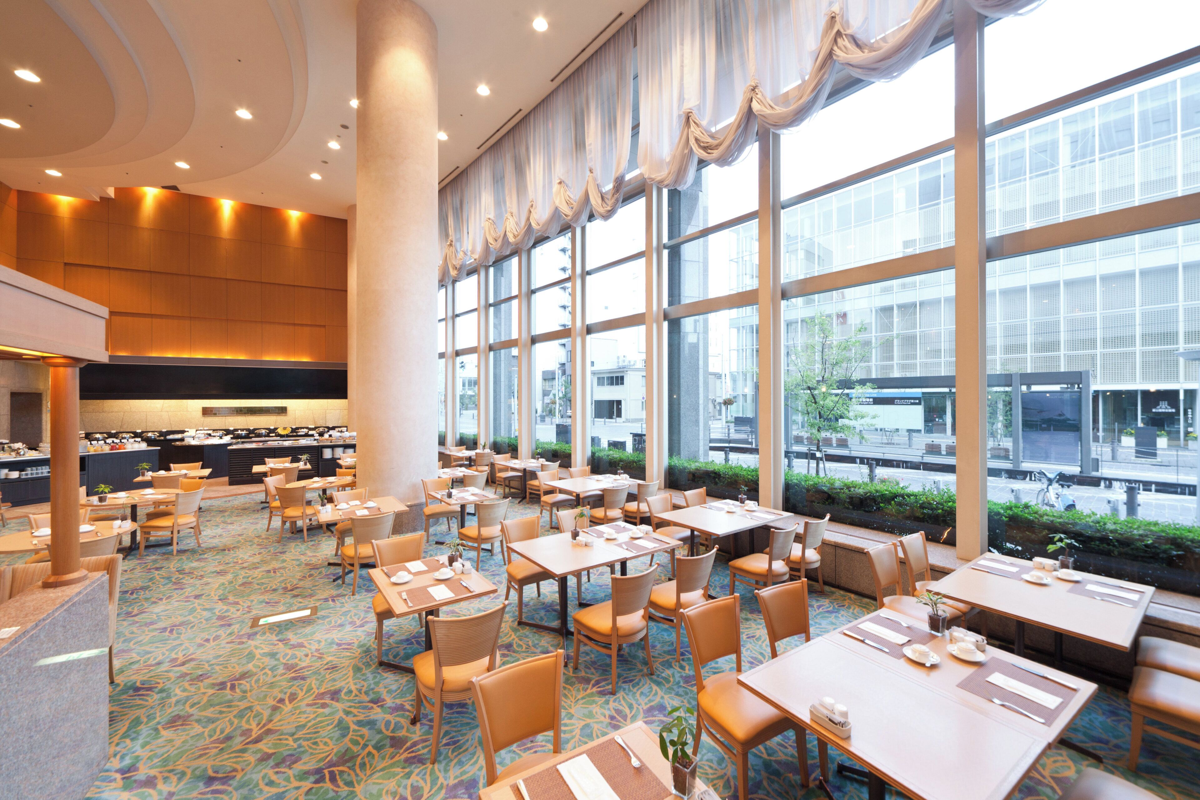 Amplia sala de comedor de hotel con múltiples mesas y sillas, ventanas grandes y una decoración de diseño moderno.