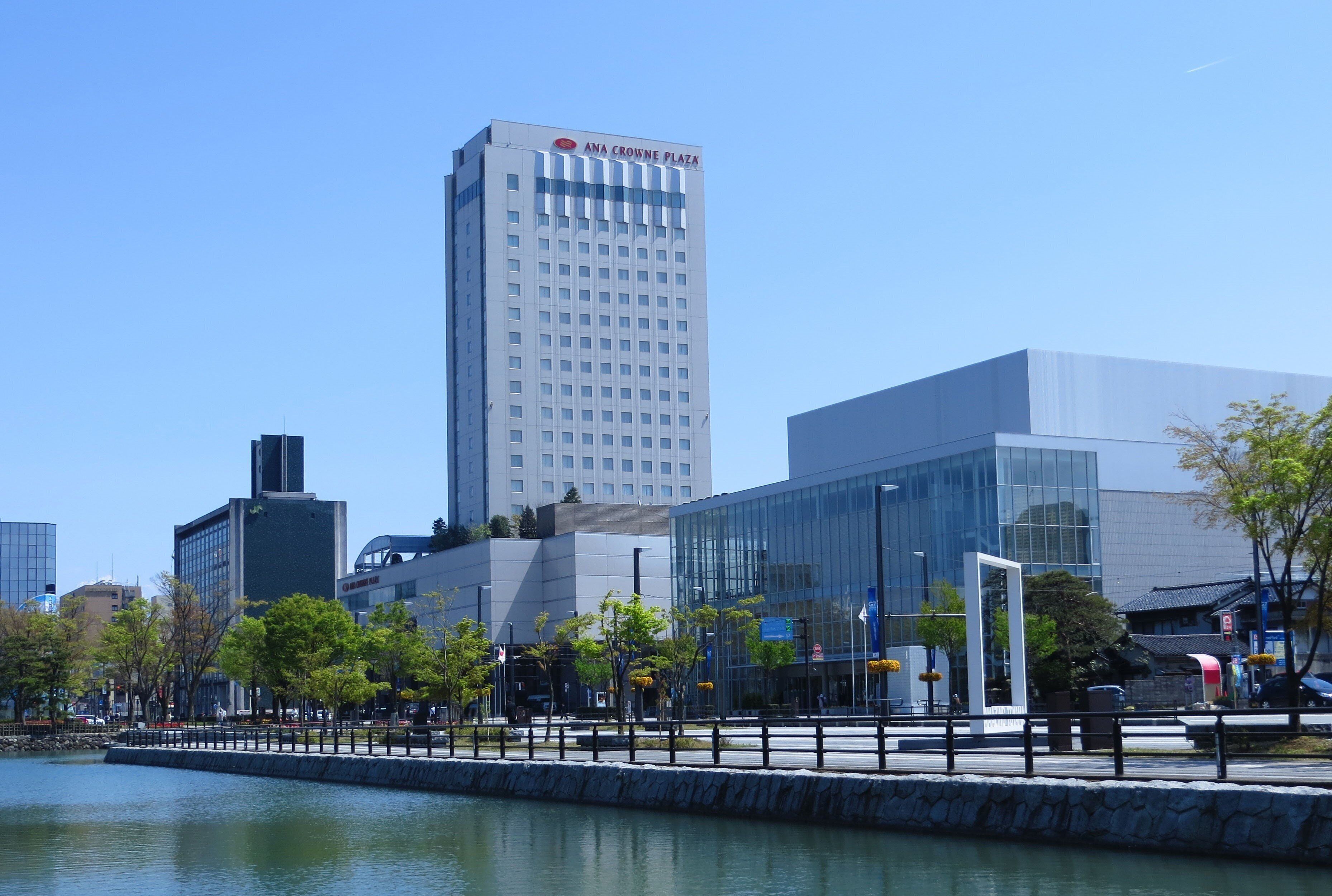 Un edificio moderno con fachada de vidrio, un letrero destacado que dice 'ANA CROWNE PLAZA' y vista al agua.