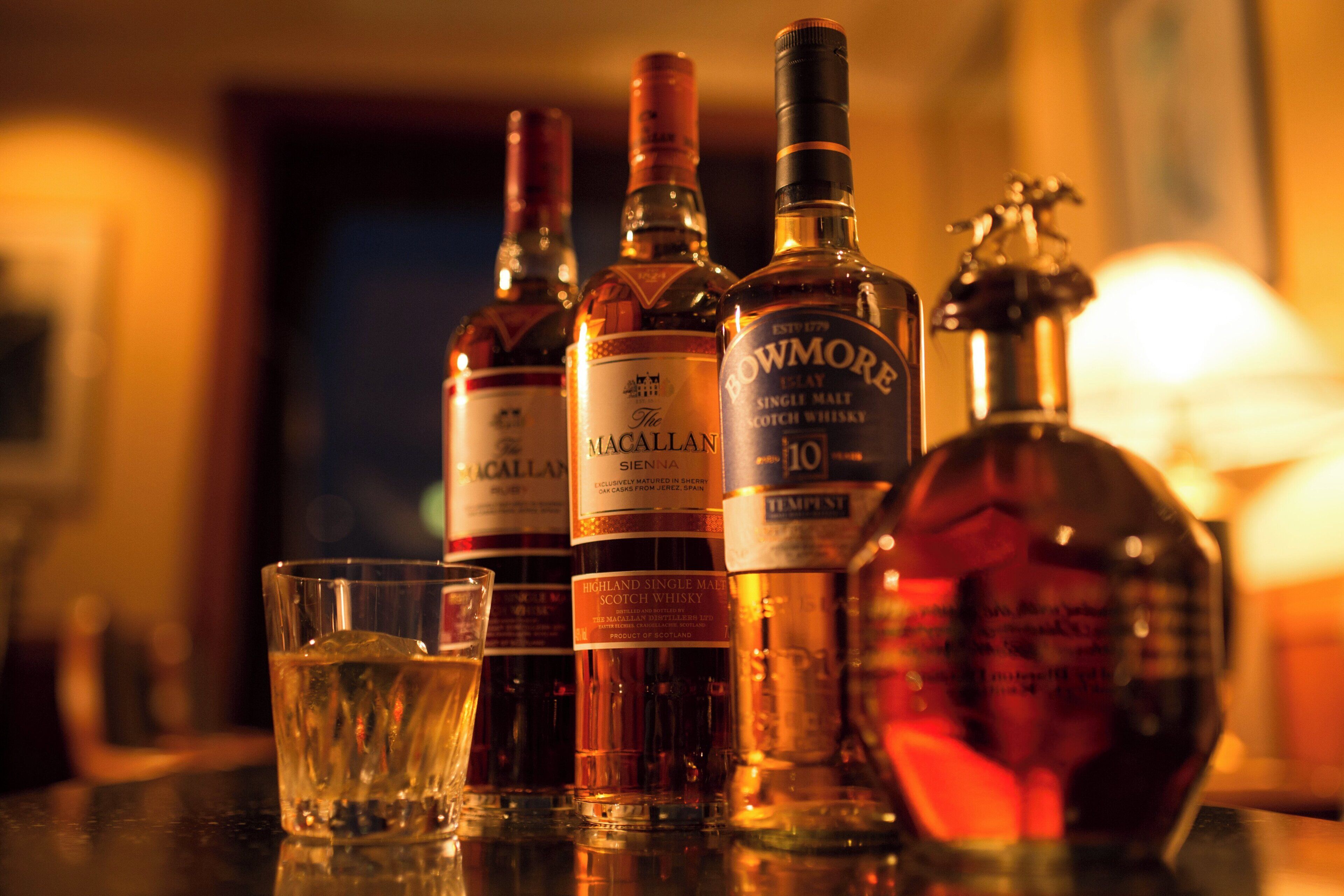 Een aantal whiskyflessen en een glas op een barkruk.