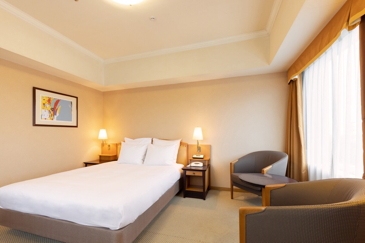 A hotel room with a large bed, two bedside tables with lamps, a chair, and a painting on the wall.