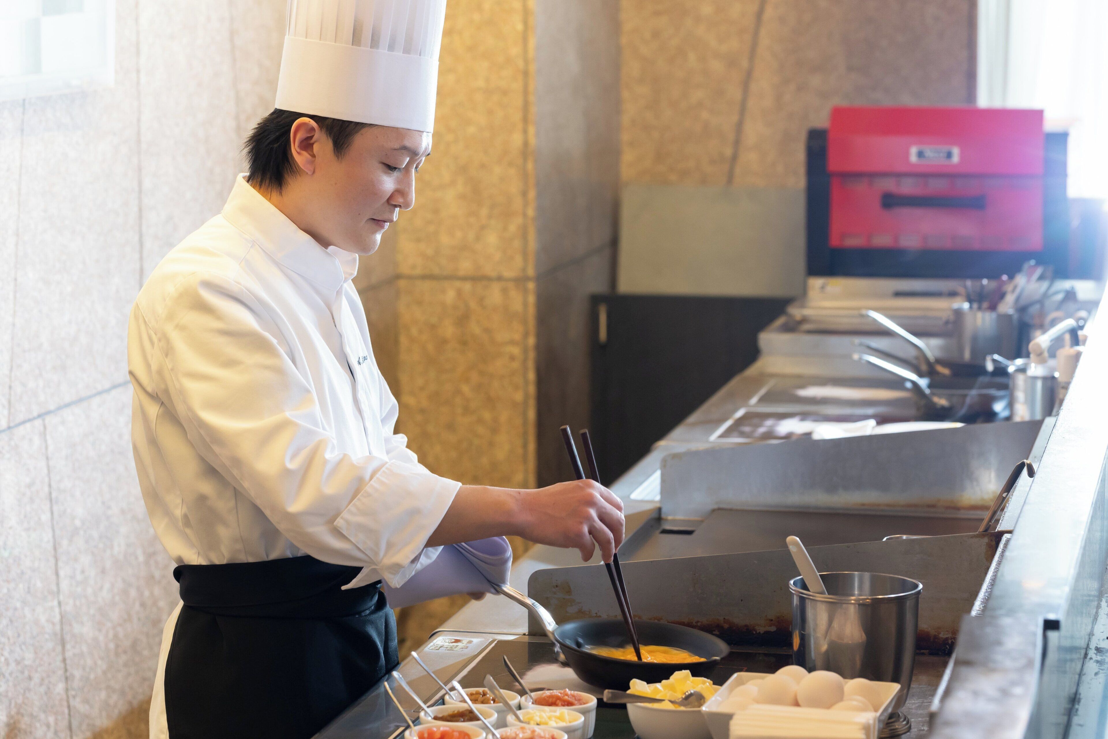 Un chef con uniforme blanco cocina usando palillos.