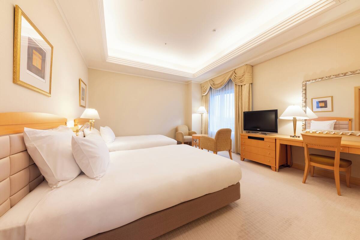 Habitación de hotel con dos camas, un escritorio, un televisor y una silla.