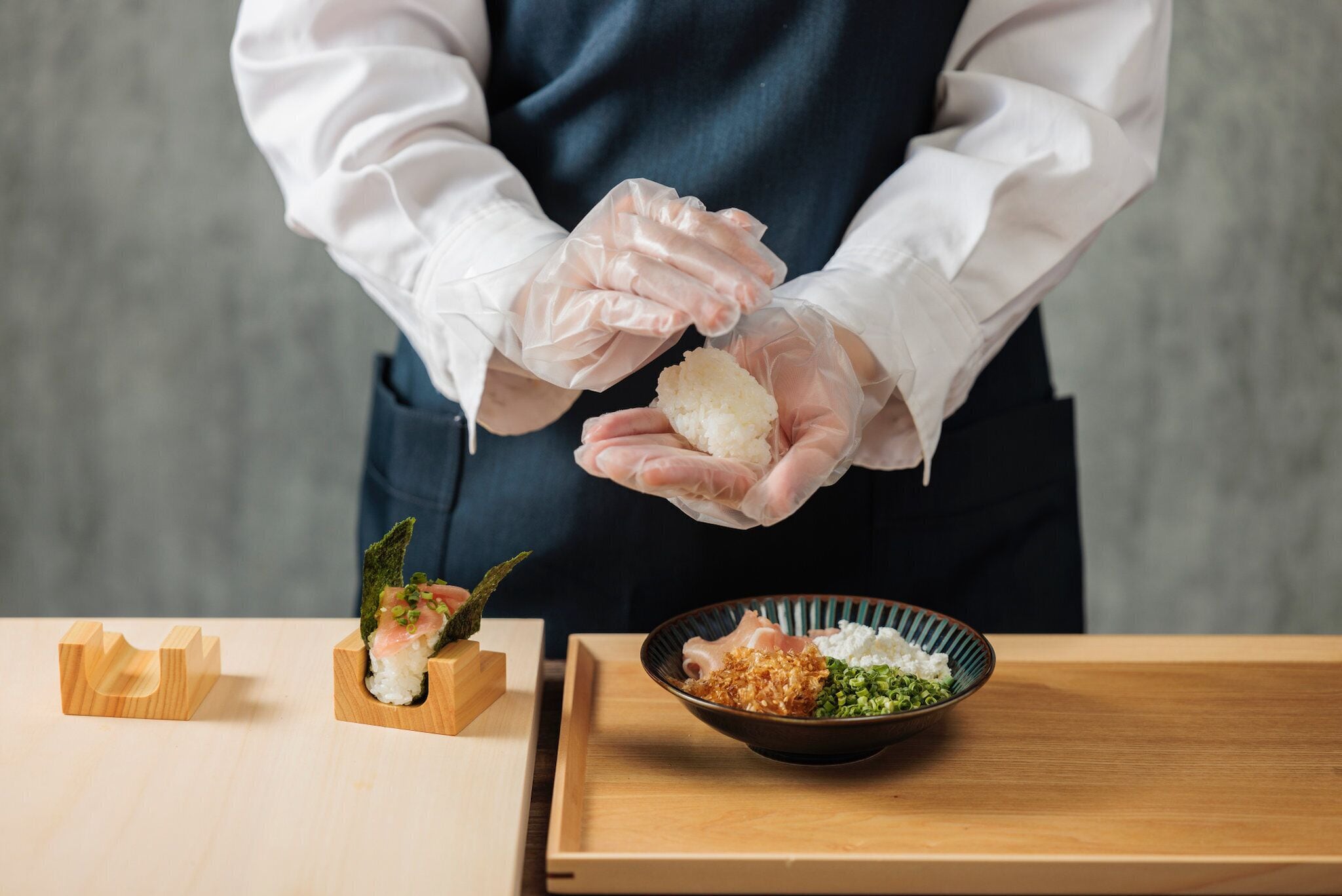A person in a white shirt and apron preparing food, with a wooden table and a bowl of ingredients.