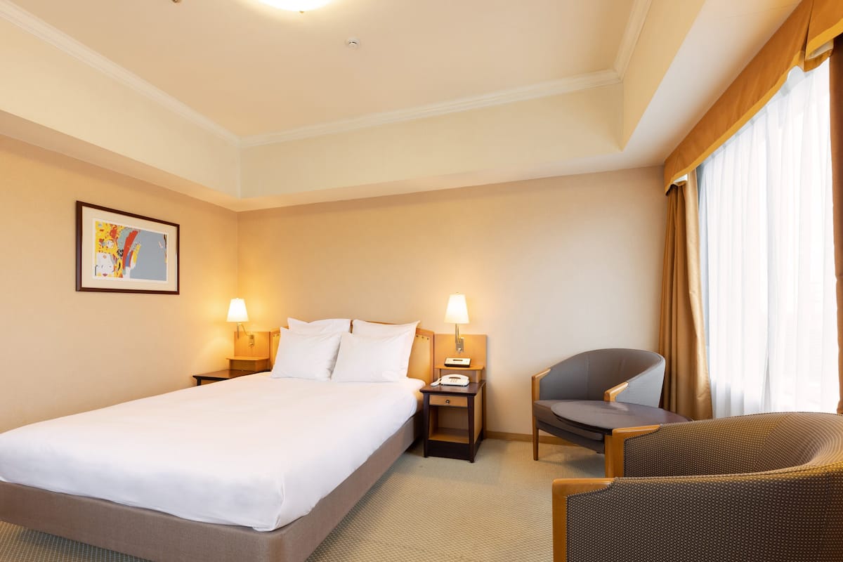 A hotel room with a large bed, two bedside tables with lamps, a chair, and a painting on the wall.