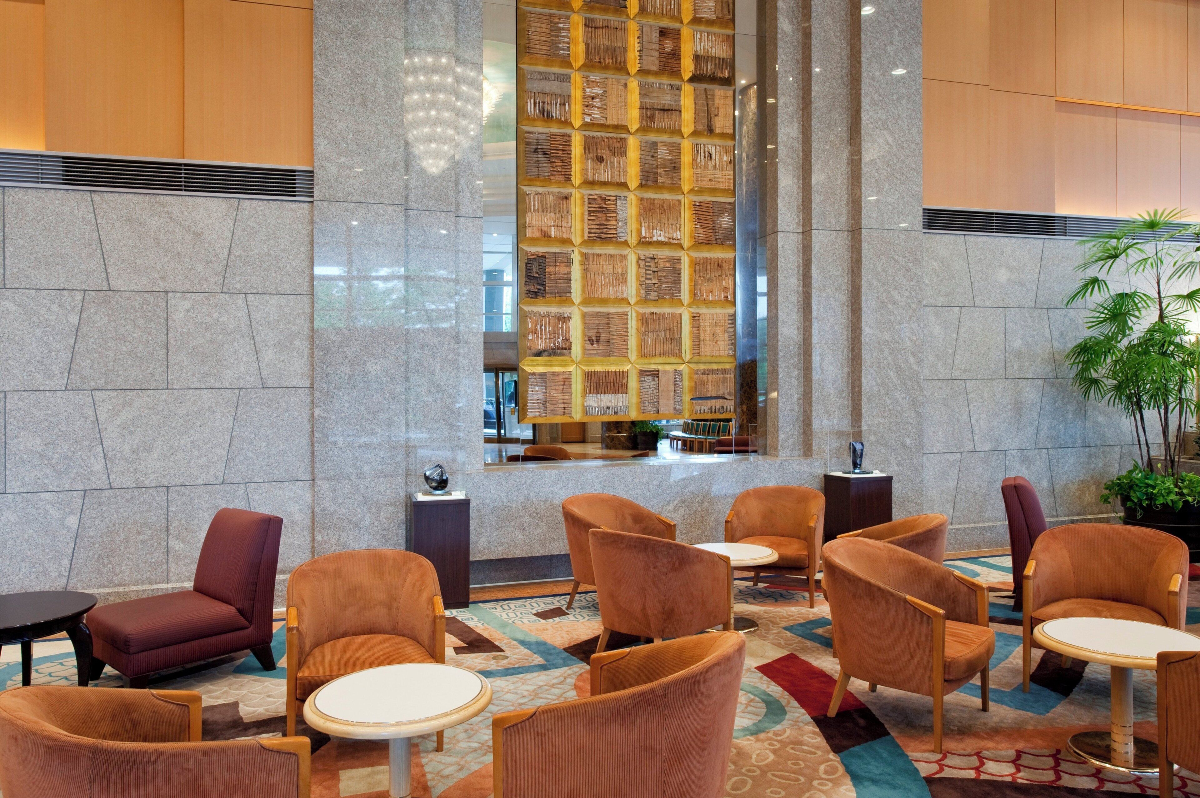 A lobby with a central seating area featuring round tables and chairs, a large decorative wall, and a potted plant.