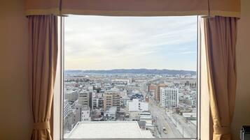 A window with curtains, a view of a cityscape, and a building with a flat roof.