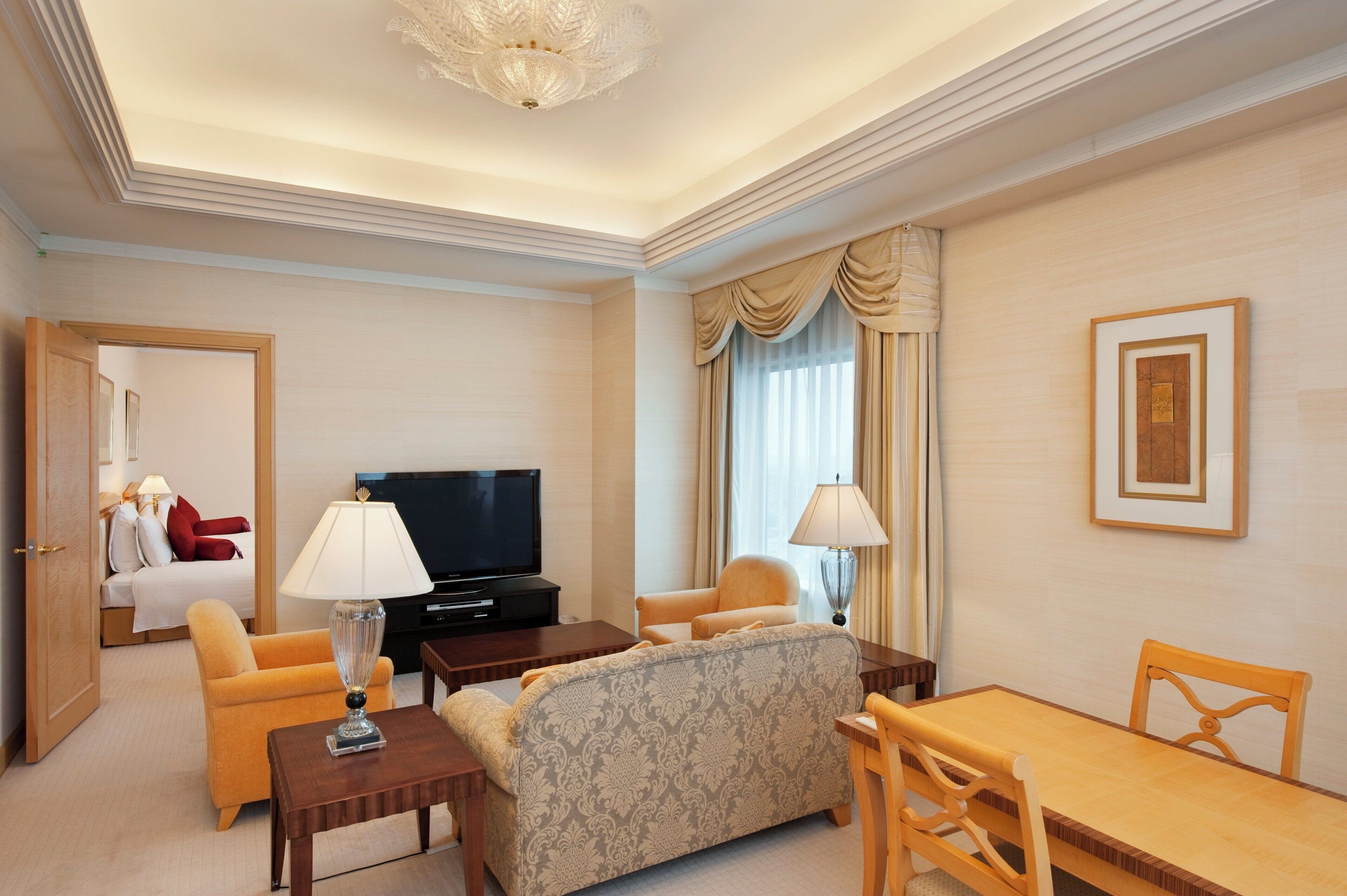 Une chambre d’hôtel équipée d’un canapé, d’un fauteuil, d’une table à manger, d’une télévision et d’un lit avec un oreiller rouge.