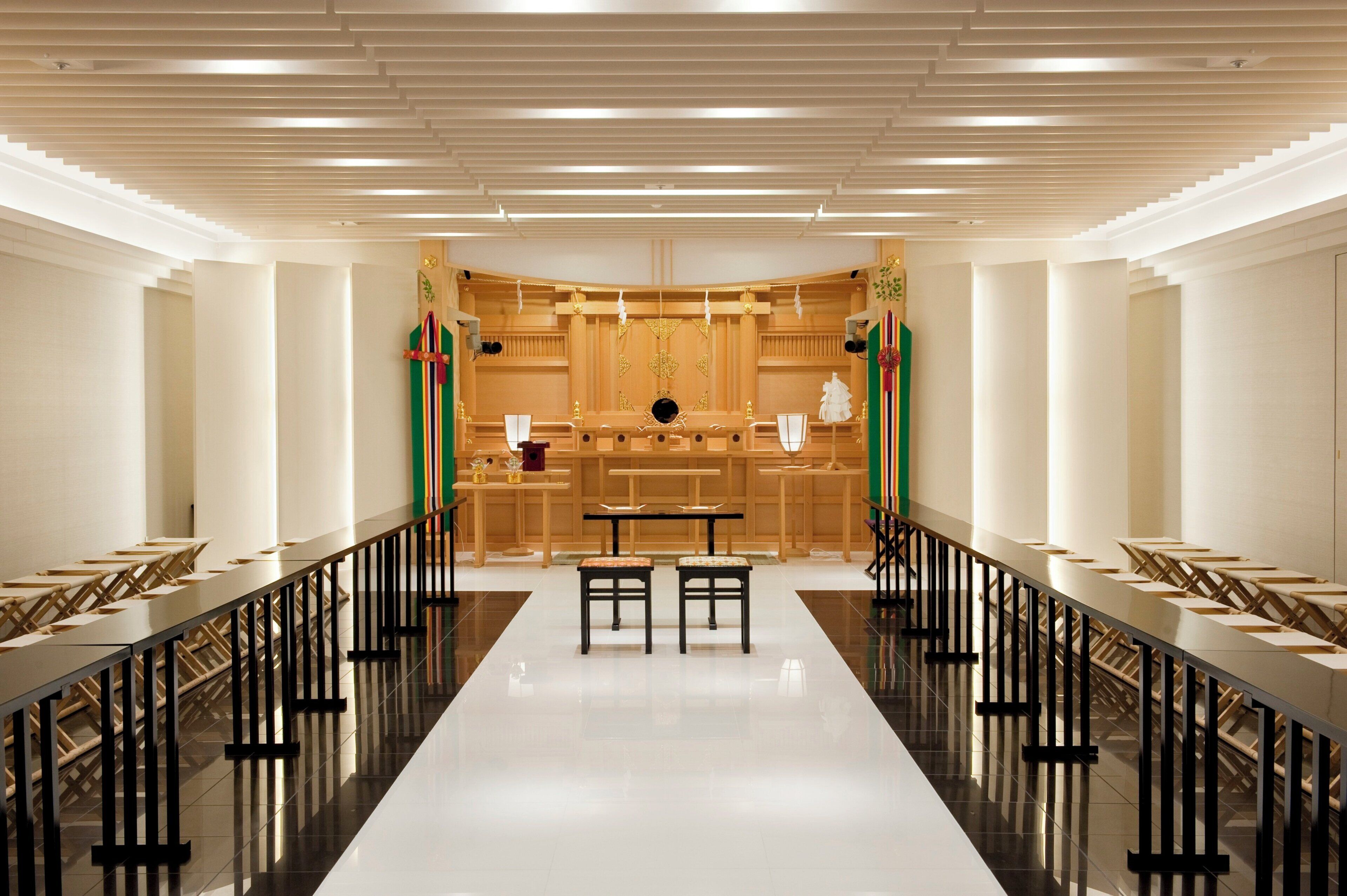 A long, narrow room with a central table and chairs, flanked by rows of tables and chairs, with a high ceiling and modern lighting.