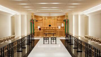 A long, narrow room with a central table and chairs, flanked by rows of tables and chairs, with a high ceiling and modern lighting.
