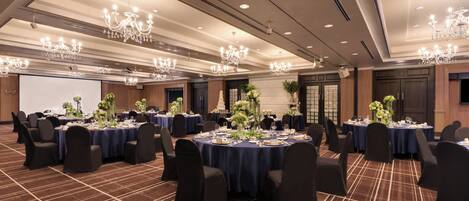 Un salón de banquetes con mesas redondas, sillas negras y candelabros.