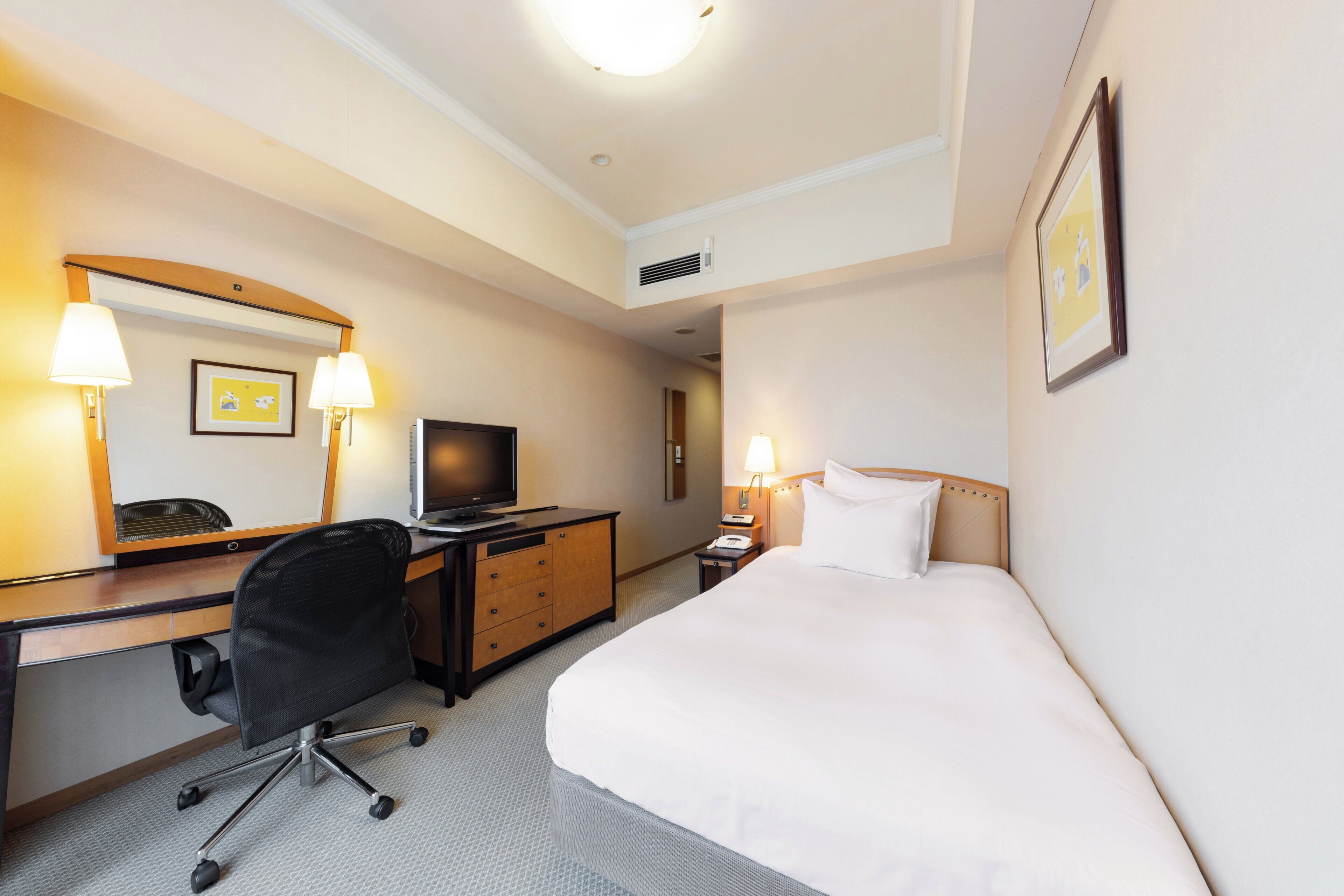 Habitación de hotel con cama, escritorio, silla, televisor y dos lámparas de noche.