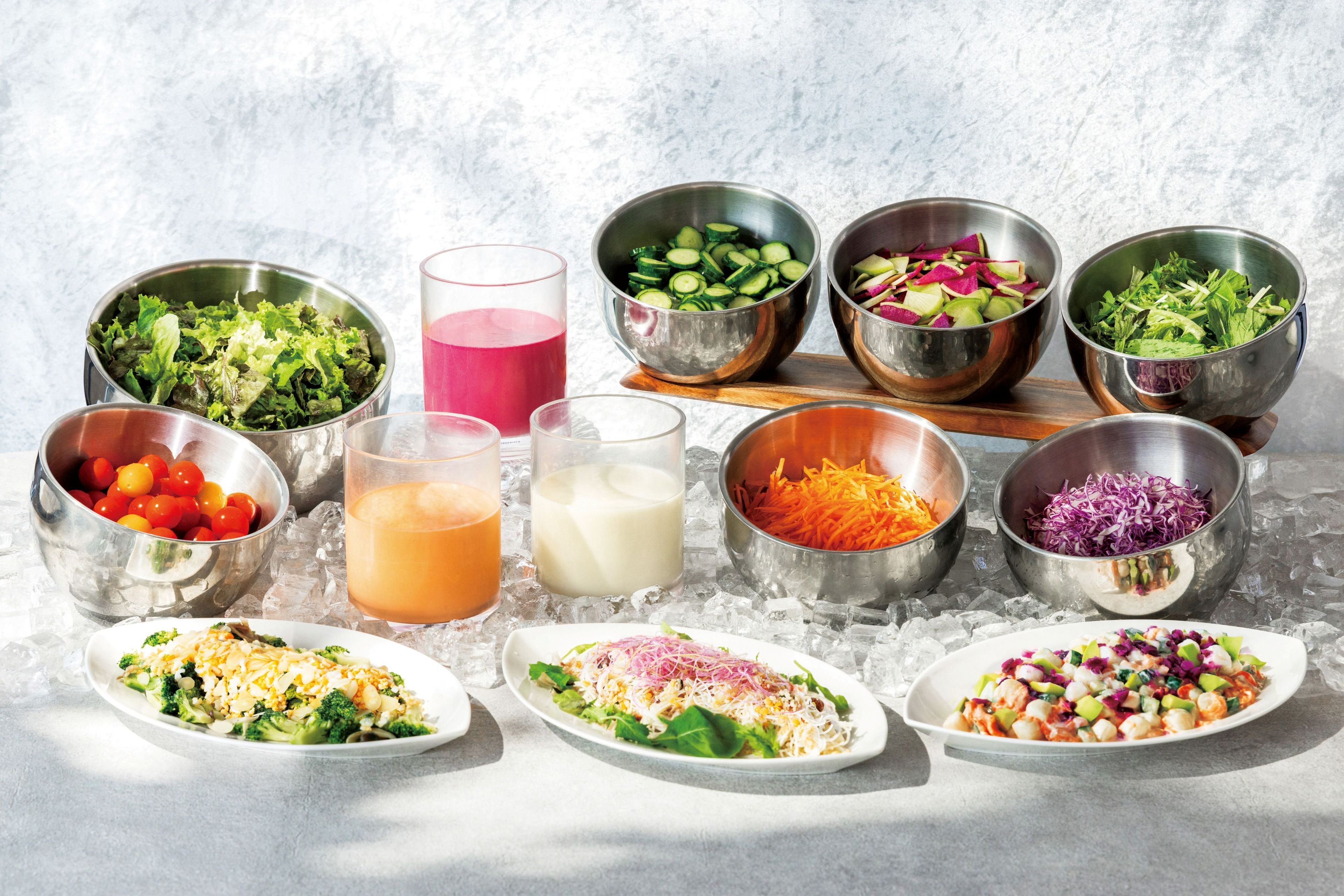 A variety of food items and drinks on a table with ice, including salads, a glass of juice, and a glass of milk.