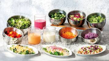 A variety of food items and drinks on a table with ice, including salads, a glass of juice, and a glass of milk.