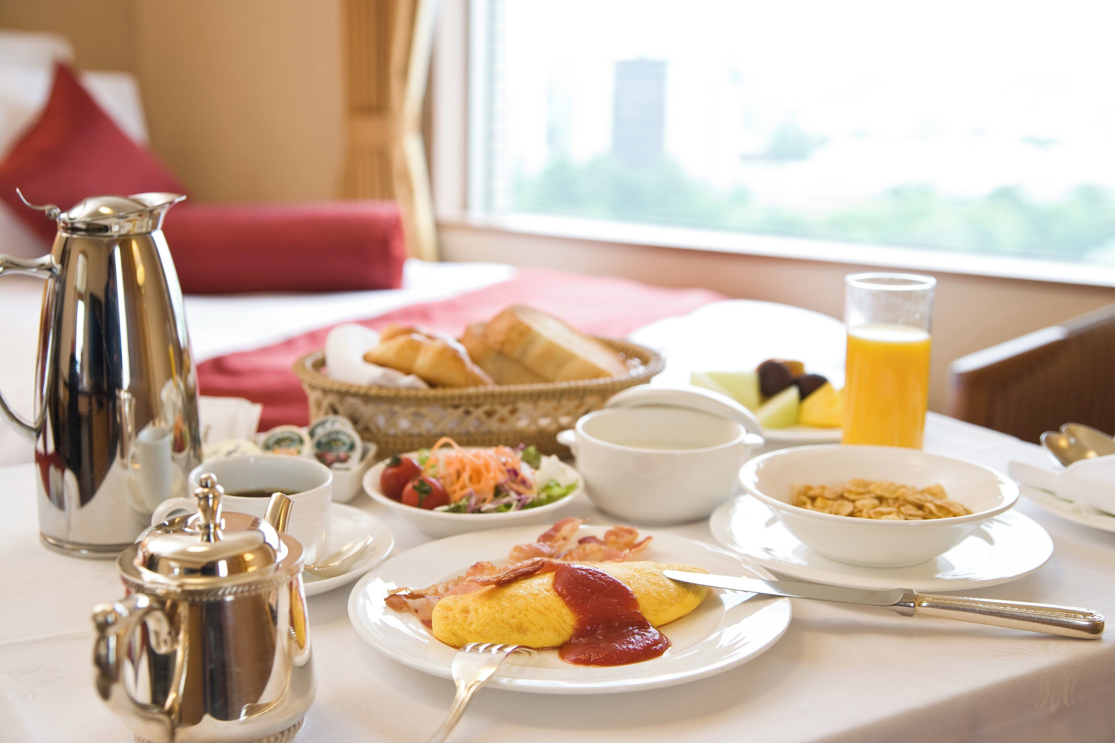 A breakfast table with various dishes, a coffee pot, and a glass of orange juice.