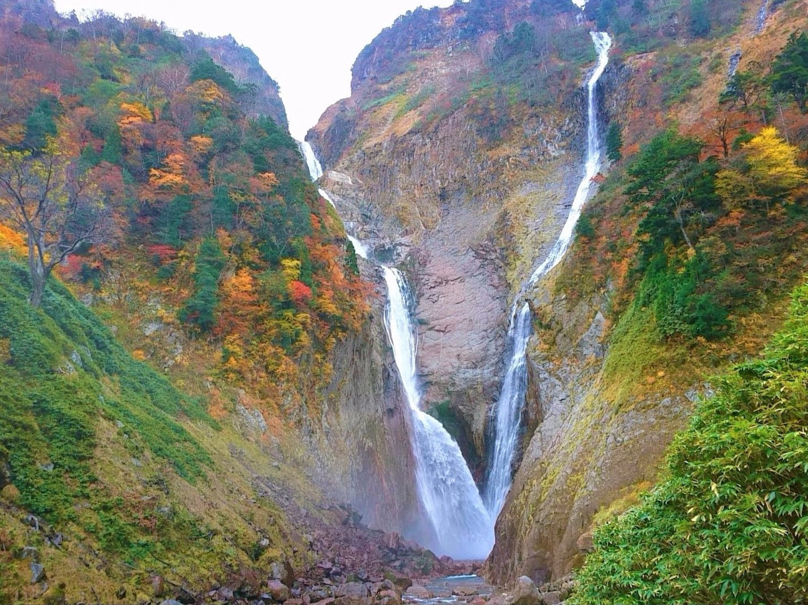Una cascada se precipita por un desfiladero rocoso, rodeado de follaje otoñal.