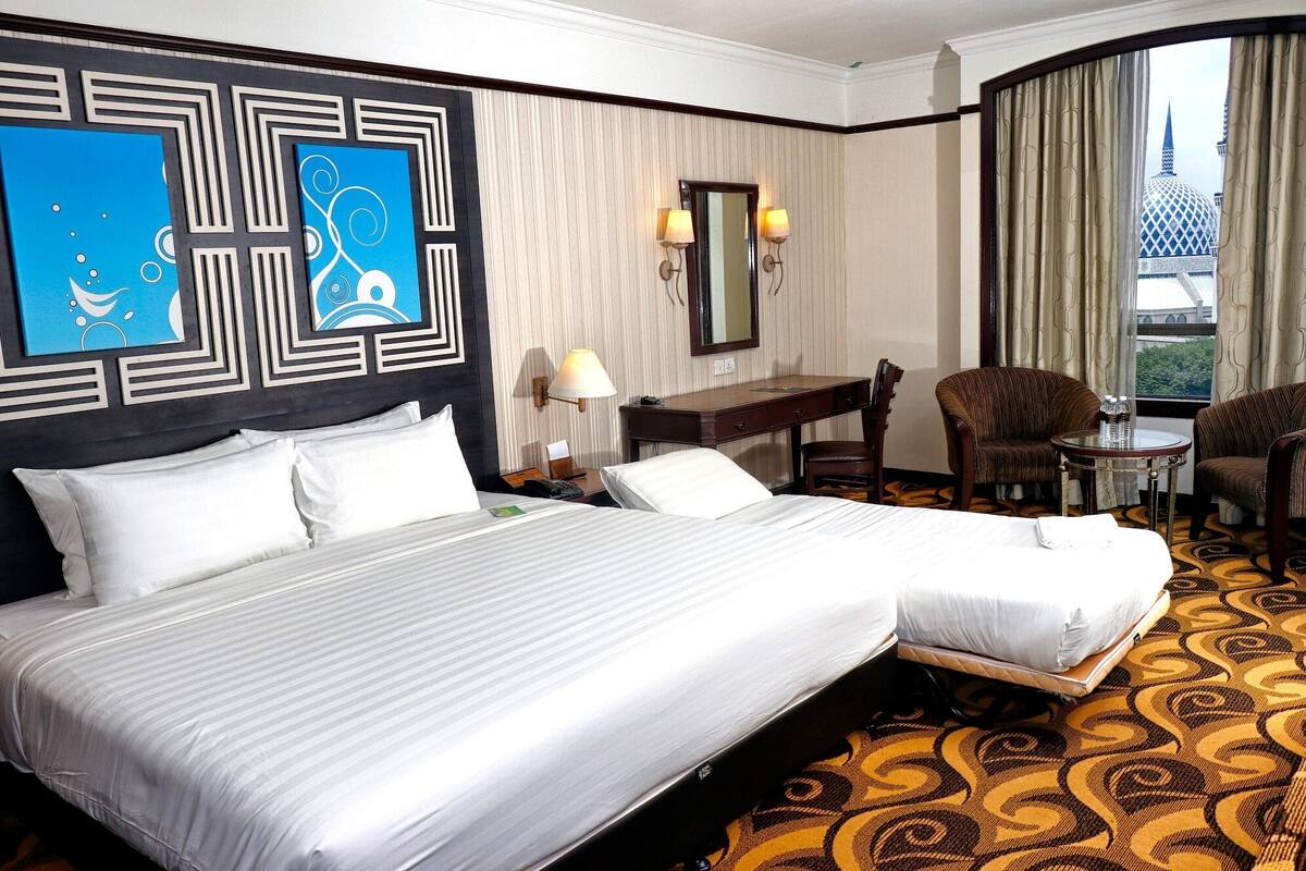 Ein Hotelzimmer mit einem großen Bett, einem Schreibtisch, zwei Stühlen, einem Spiegel und Blick auf ein Gebäude mit einer Kuppel.