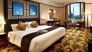 A hotel room with a large bed, a desk, a chair, and a view of a mosque through the window. - Mardhiyyah Hotel and Suites (Shah Alam)