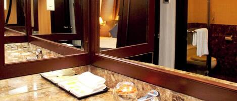Un baño de hotel con lavamanos de mármol, un cuenco de vidrio y un espejo que refleja la habitación.